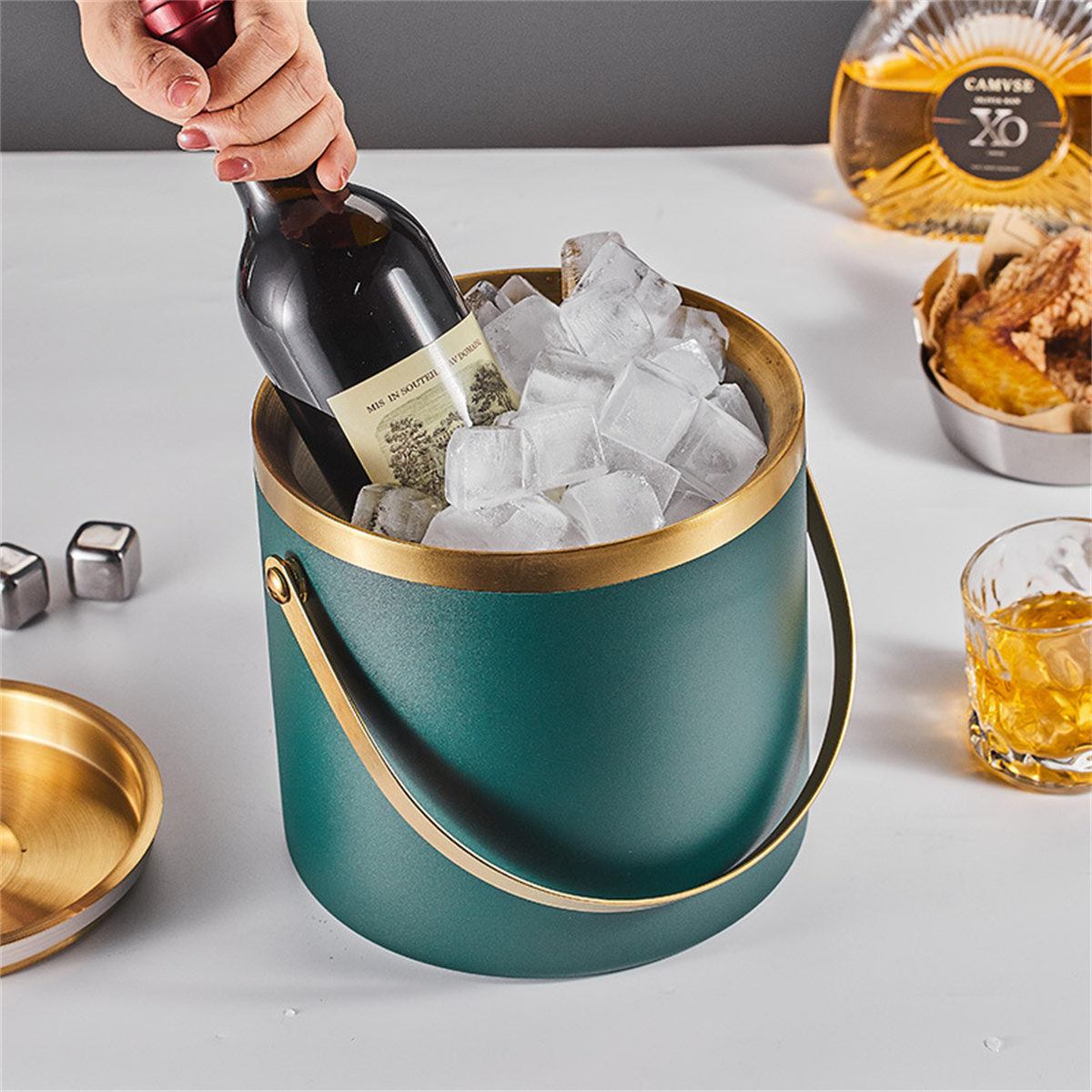 Eine Person stellt eine Weinflasche in einen Eiskübel. Weitere Gegenstände sind ein Glas, Snacks und Schnaps.