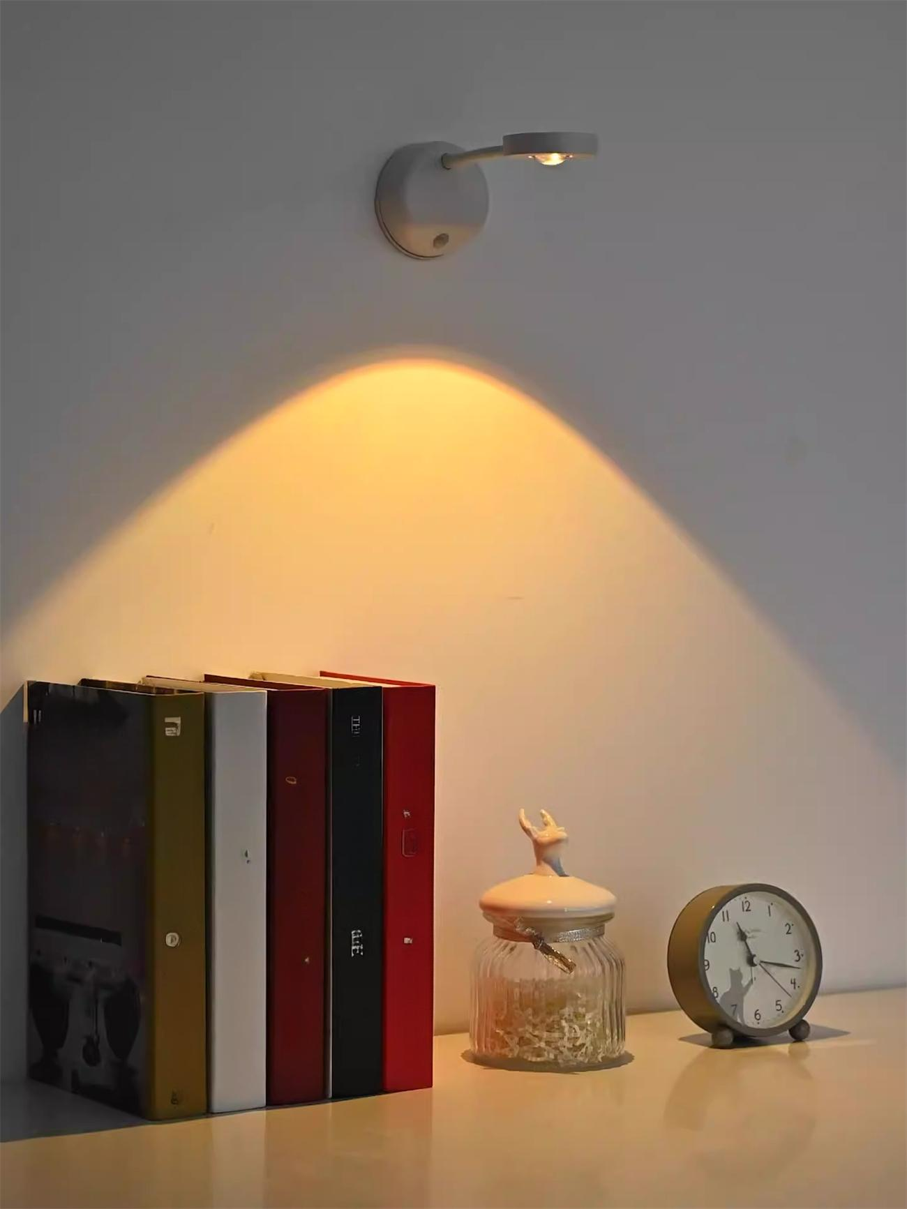 Bücher, eine Uhr und ein Glas stehen auf einem Regal. Ein Licht scheint herunter. Der Hintergrund ist eine weiße Wand.