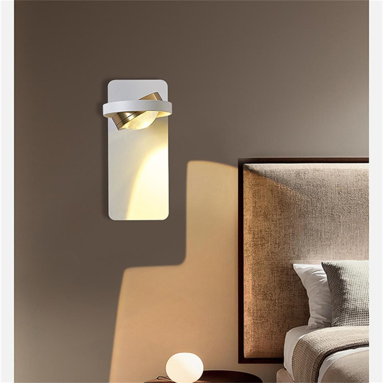 Weiße Wandlampe mit goldenen Akzenten, die eine Schlafzimmereinstellung beleuchtet. Ein Bett mit Kissen und eine Lampe sind sichtbar.