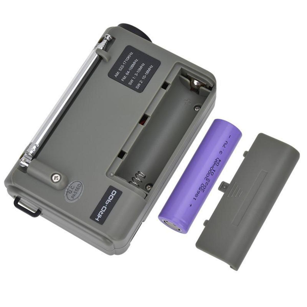 Ein graues Radio mit offenem Batteriefach, eine violette Batterie und eine abgenommene Abdeckung liegen auf einer weißen Oberfläche.
