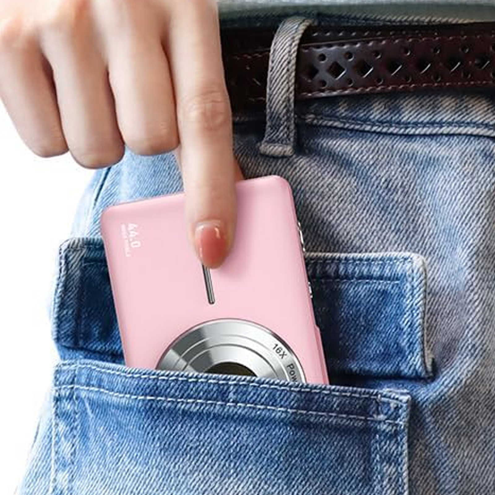 Eine Hand legt eine rosa Kamera in eine Jeanstasche. Ein Gürtel und Denim sind sichtbar.