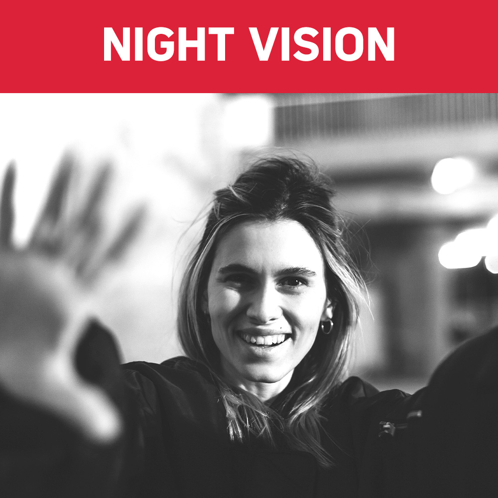 Uśmiechnięta kobieta wyciąga rękę w stronę widza. Obraz jest czarno-biały. Tekst 'NIGHT VISION' znajduje się u góry.
