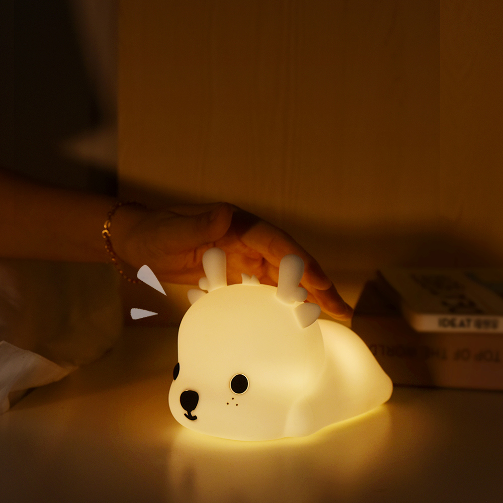 Eine leuchtende, hirschförmige Lampe steht auf einem Tisch. Eine Hand schwebt darüber. Im Hintergrund ist ein Buch zu sehen.
