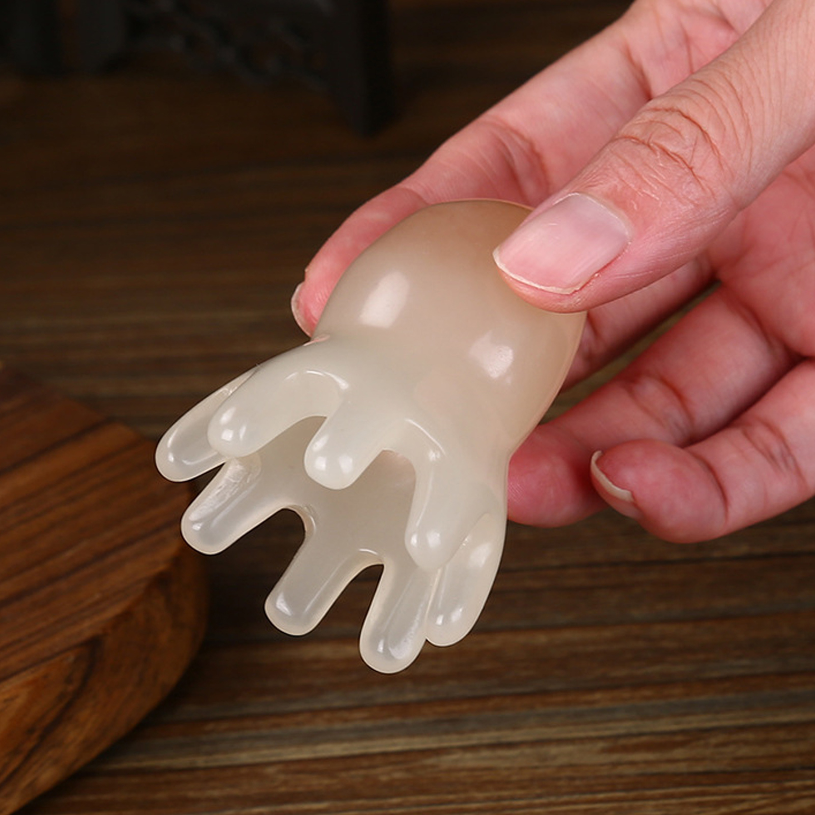Eine Hand hält ein weißes, handförmiges Massagegerät. Der Hintergrund ist eine Holzoberfläche.