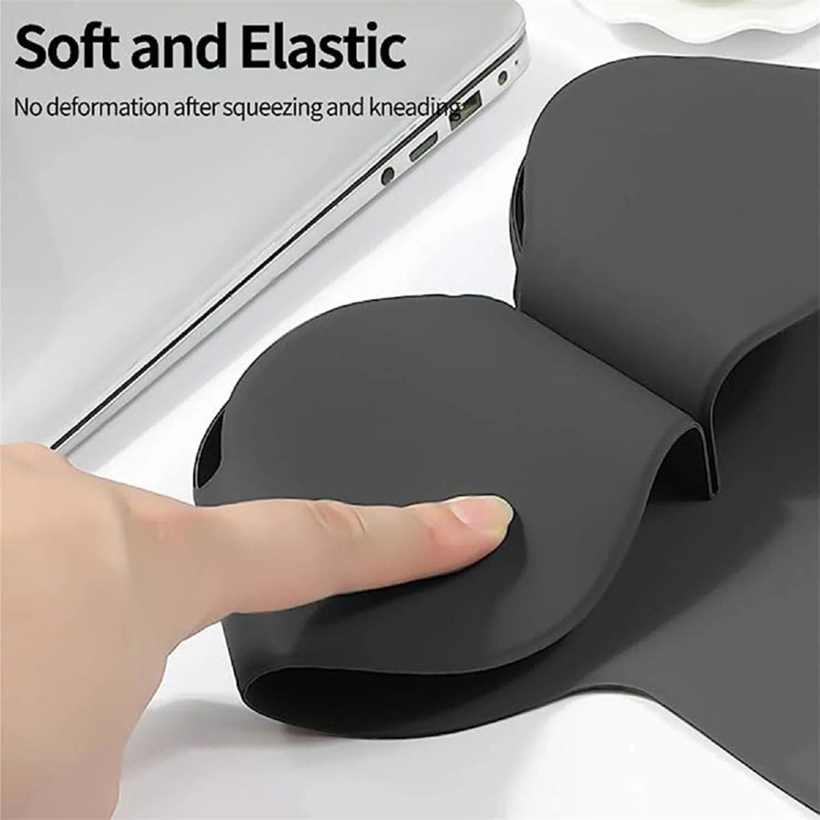 Eine Hand drückt einen Finger auf eine schwarze, weiche und elastische Oberfläche. Ein Laptop ist im Hintergrund.
