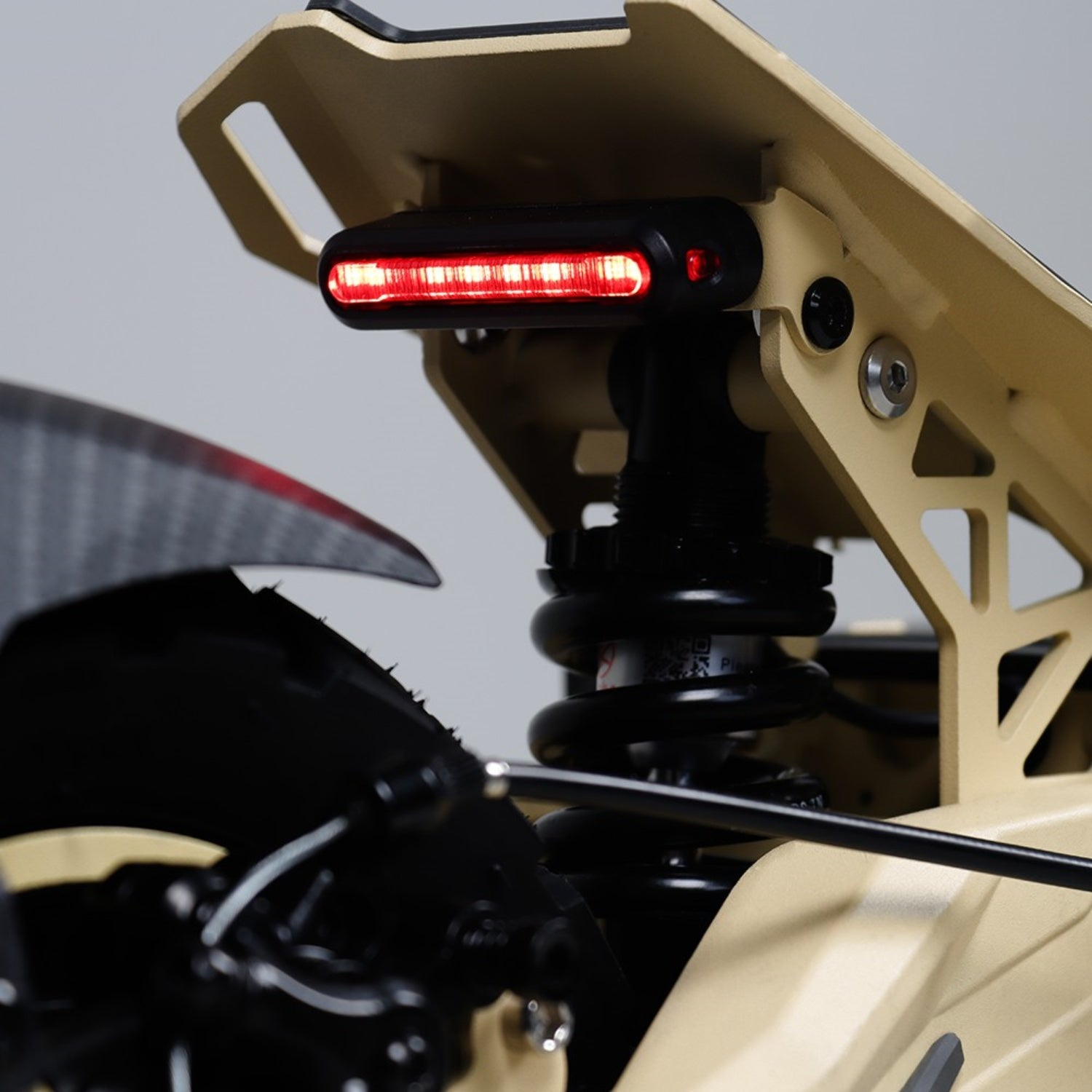 Primo piano della parte posteriore di uno scooter. Mostra una luce freno rossa, un telaio beige, un ammortizzatore nero e parte dello pneumatico.