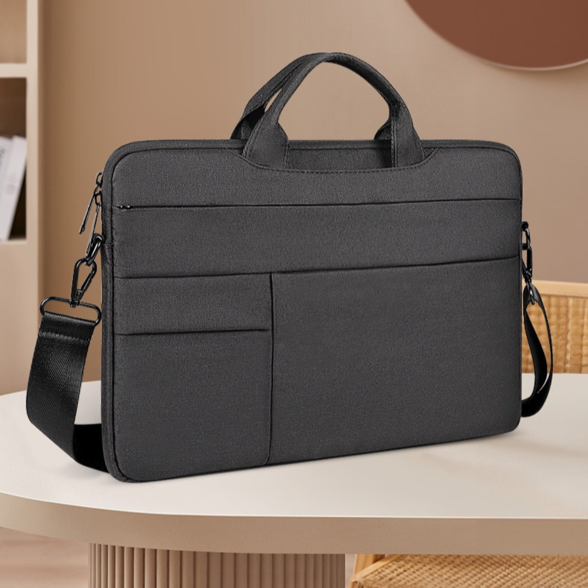 Eine schwarze Laptoptasche mit Griff und Schulterriemen steht auf einem Tisch. Im Hintergrund sind ein Regal und eine Wand zu sehen.