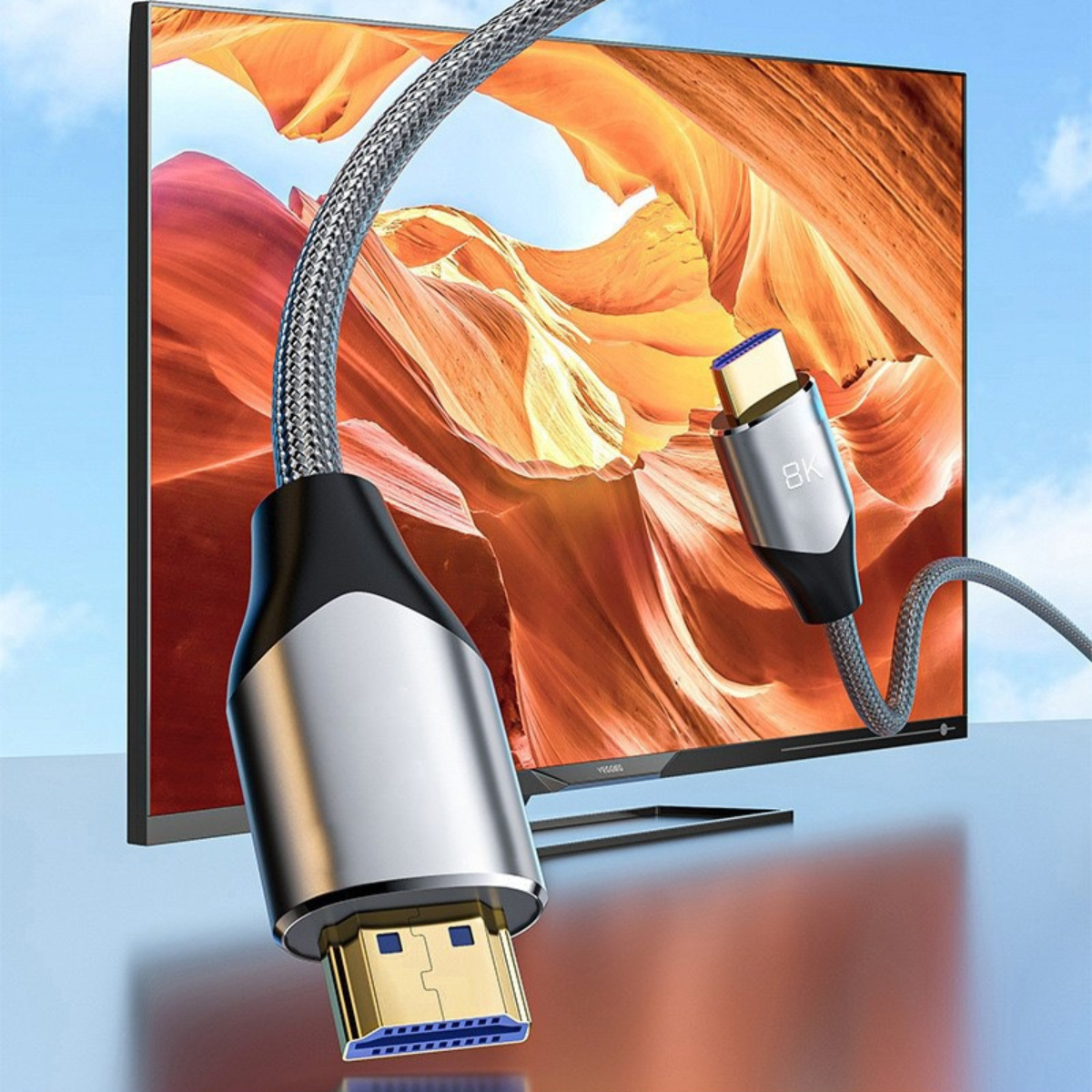 HDMI-Kabel mit goldenen und silbernen Steckern. Ein Fernseher zeigt im Hintergrund ein Landschaftsbild vor blauem Himmel.