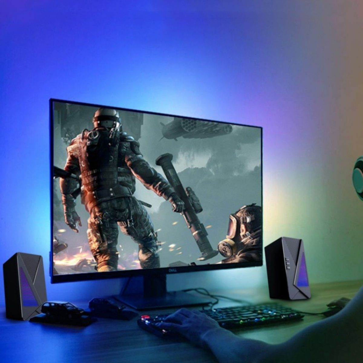 Eine Person spielt. Ein Monitor zeigt einen Soldaten mit einer Waffe. Lautsprecher, Tastatur und Maus stehen auf einem Schreibtisch. Blaue und violette Beleuchtung.