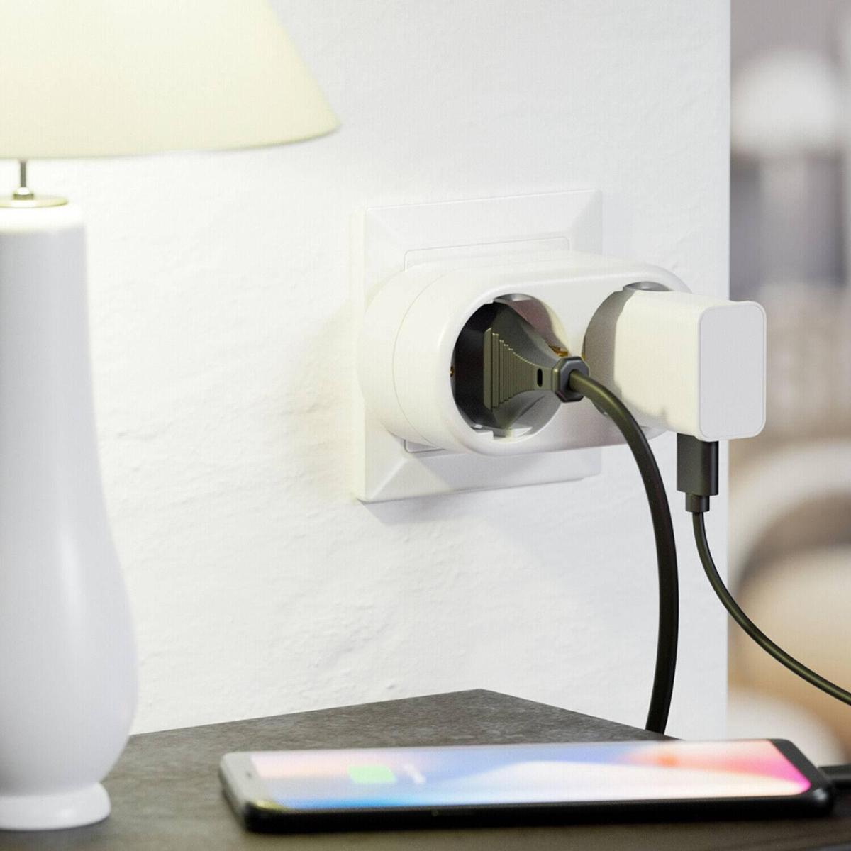 Weiße Wand mit Steckdose, die ein Telefon und eine Lampe auflädt. Ein Telefon lädt auf einem Tisch.