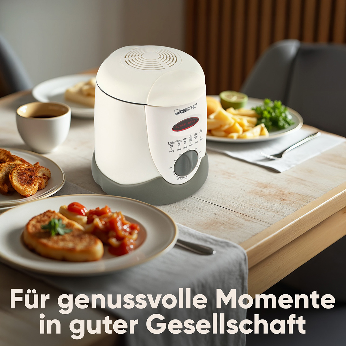 Biała frytownica na stole z talerzami jedzenia. Widoczna jest również filiżanka kawy i szare krzesło.