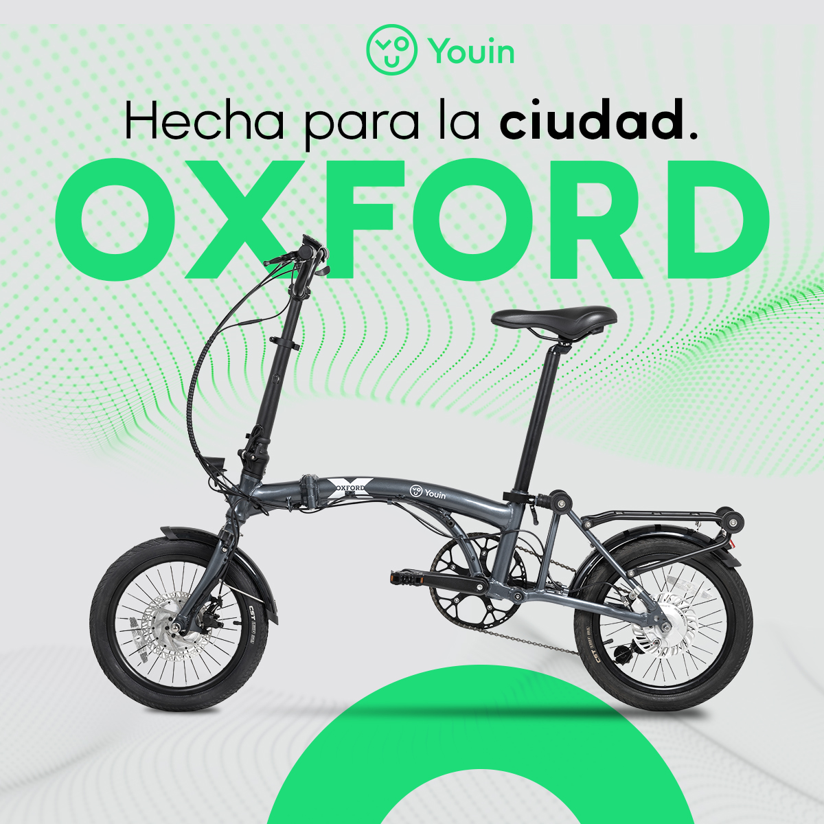 Se muestra una bicicleta plegable Oxford gris. El fondo presenta acentos verdes y el texto: 'Hecha para la ciudad. OXFORD.'