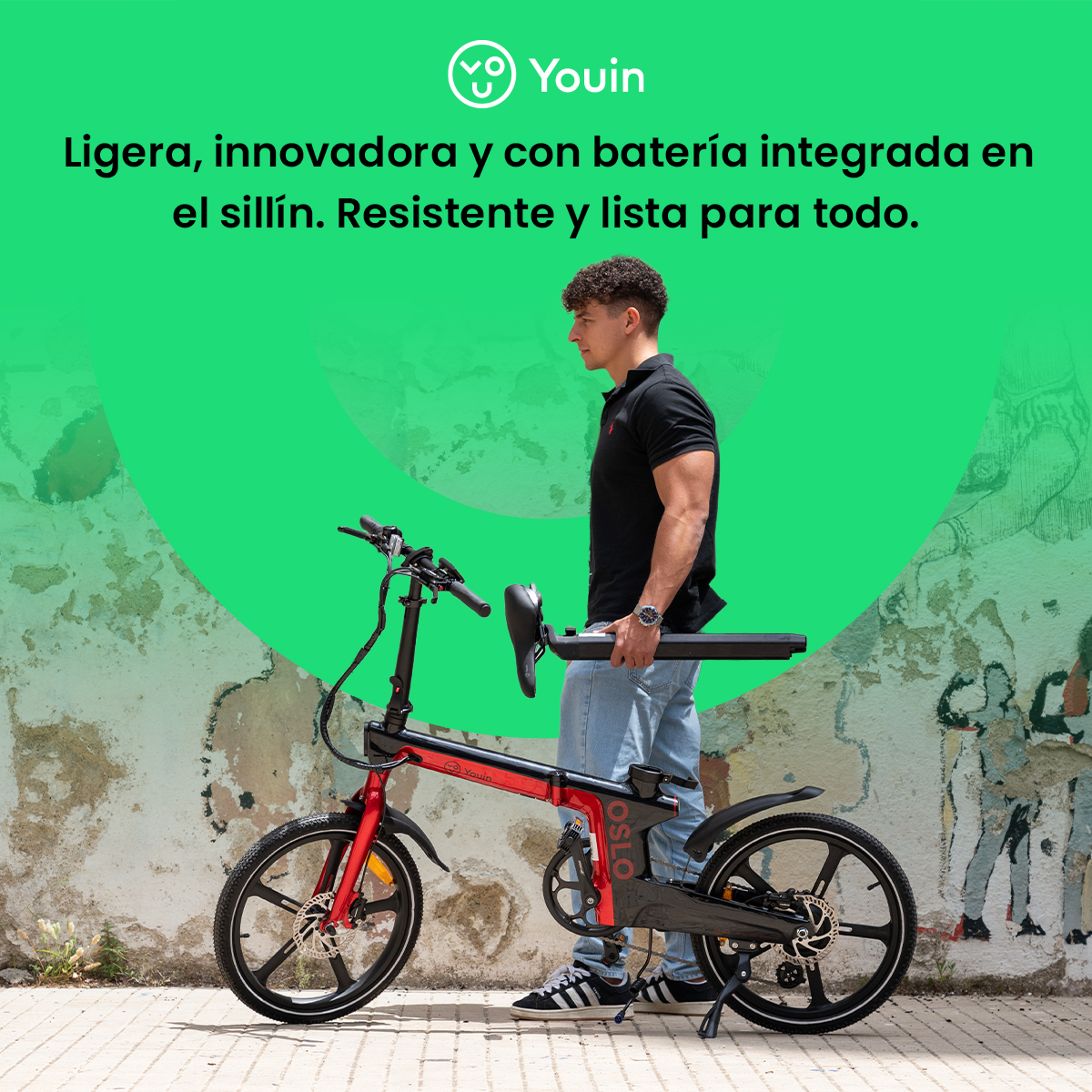 Hombre sostiene una bicicleta eléctrica plegable roja y negra. El fondo tiene un círculo verde y una pared desgastada.