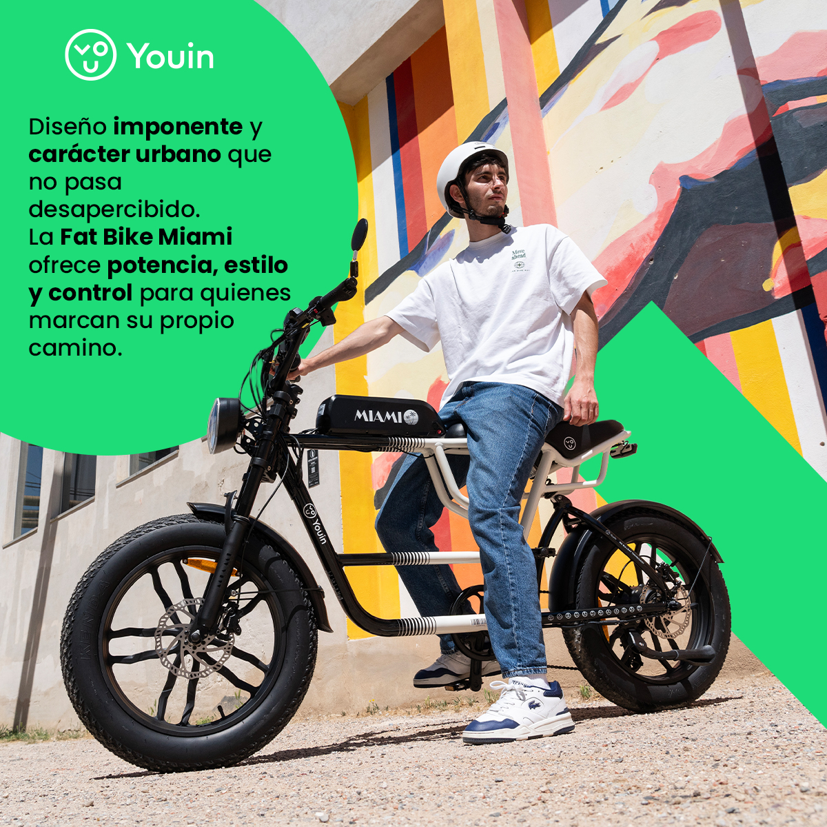 Hombre en una Youin Fat Bike Miami con casco blanco. El fondo es un mural colorido. La bicicleta es negra y blanca.