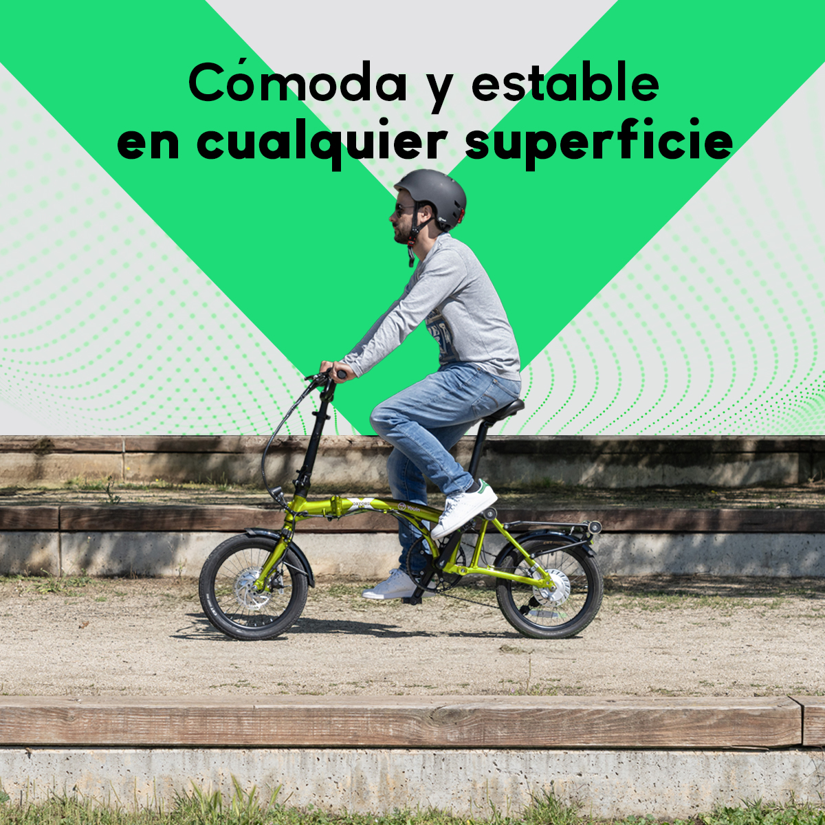 Un hombre monta en bicicleta plegable verde en un camino de grava. Texto en español: Cómodo y estable en cualquier superficie.