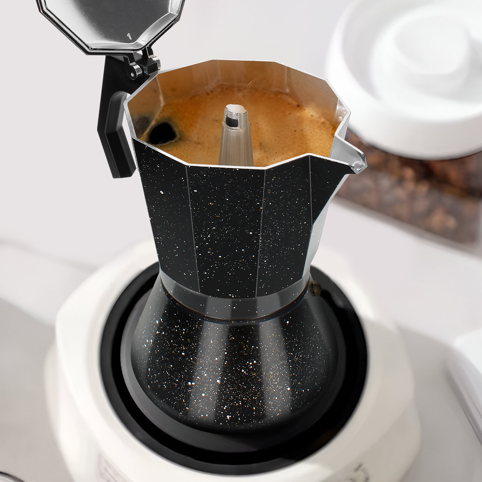 Schwarzer und silberner Espressokocher, der Kaffee auf einem weißen Herd brüht. Kaffeebohnen in einem transparenten Behälter im Hintergrund.