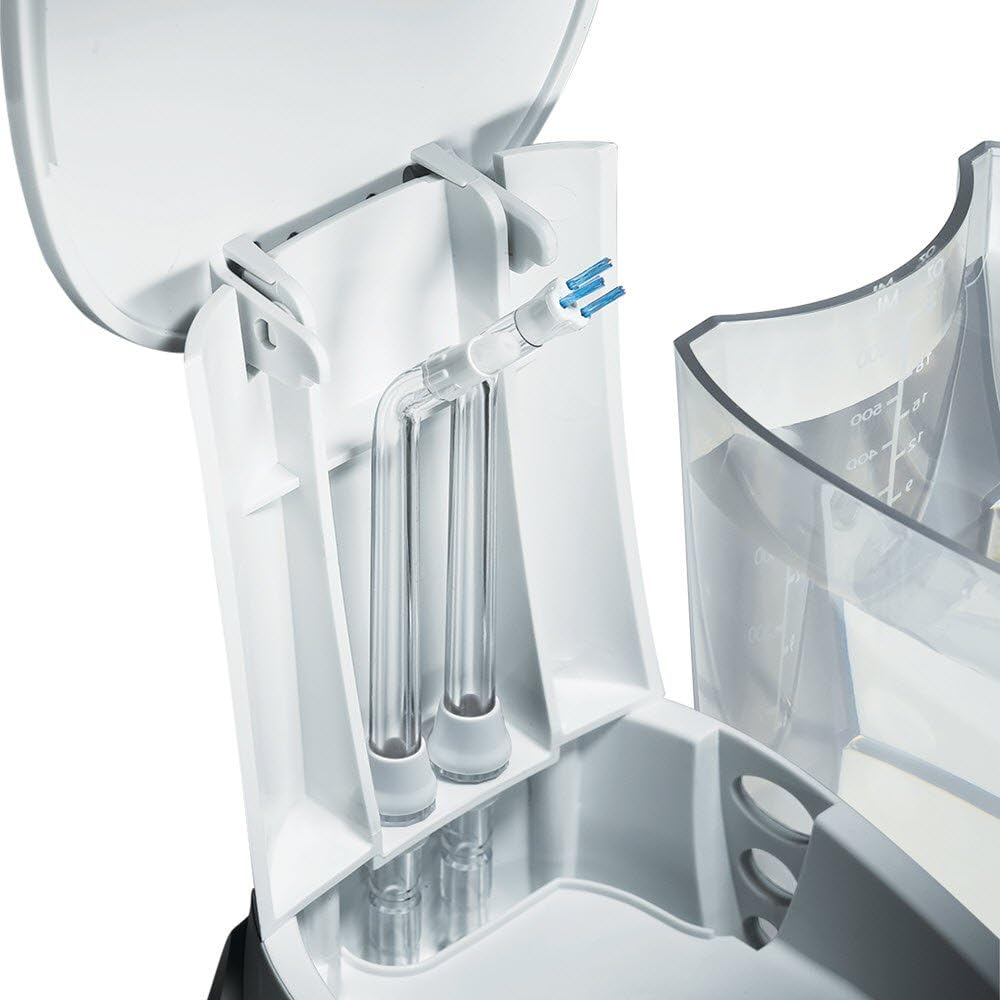 Irrigador dental blanco con puntas azules, tubos transparentes y depósito de agua. Partes blancas y transparentes. Tapa abierta.