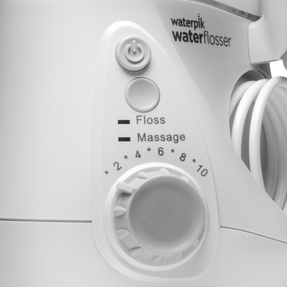 Panel de control blanco del irrigador Waterpik. Botones de encendido, hilo dental, masaje y dial de intensidad. Manguera de agua visible.