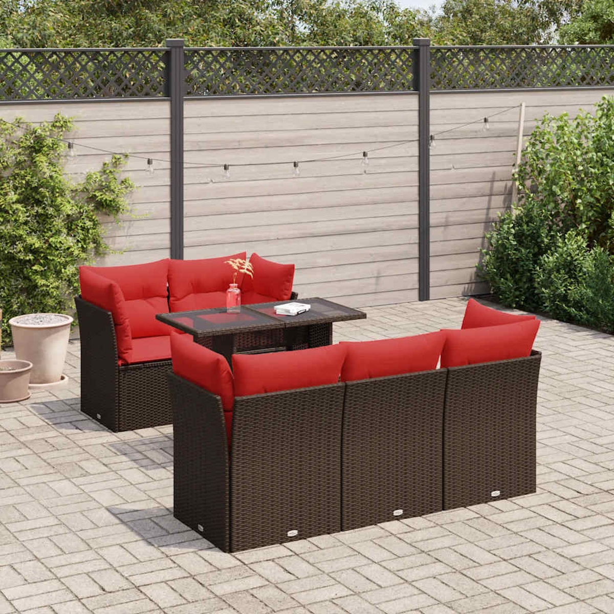 Terrassenmöbel-Set: braune Korbsessel mit roten Kissen und Tisch. Hintergrund: Zaun und Pflanzen.