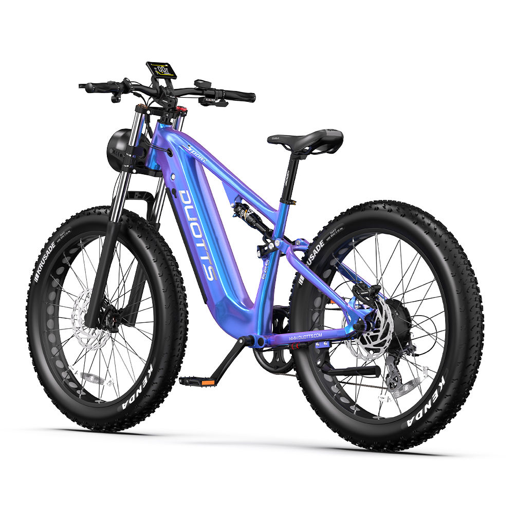 Una bicicleta eléctrica moderna con cuadro azul-púrpura, neumáticos anchos negros y pantalla digital. Está sobre fondo blanco.