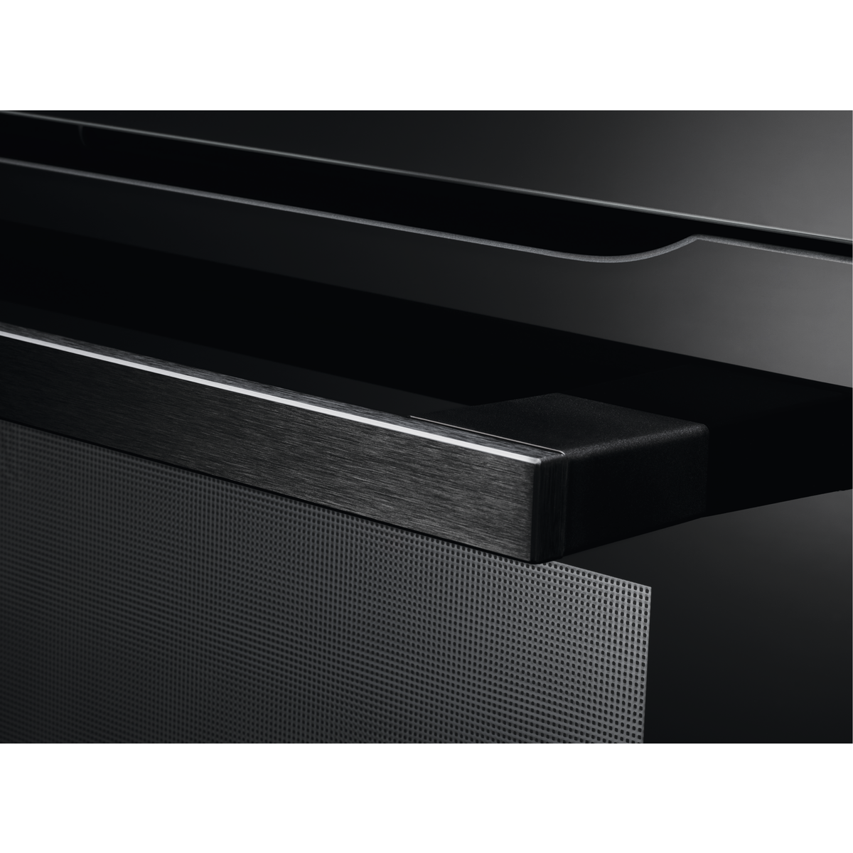 Primer plano de un electrodoméstico negro con un asa metálica y una superficie perforada. El fondo es oscuro y borroso.