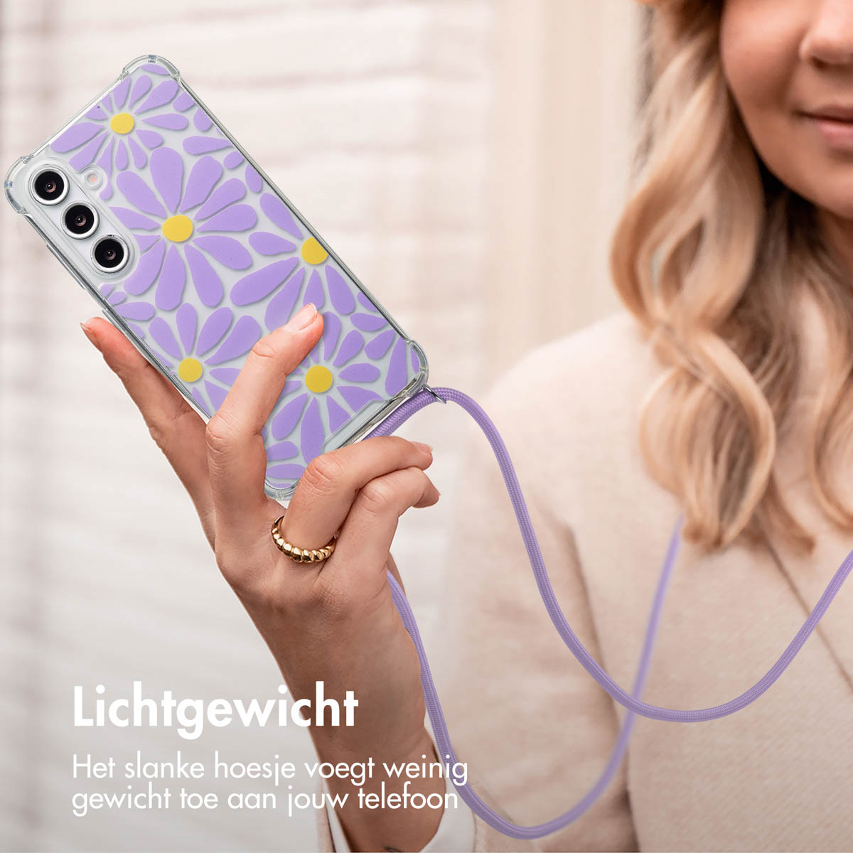 Une femme tient un téléphone dans un étui à marguerites, mains libres, avec un cordon violet. Elle porte une bague et un haut beige.