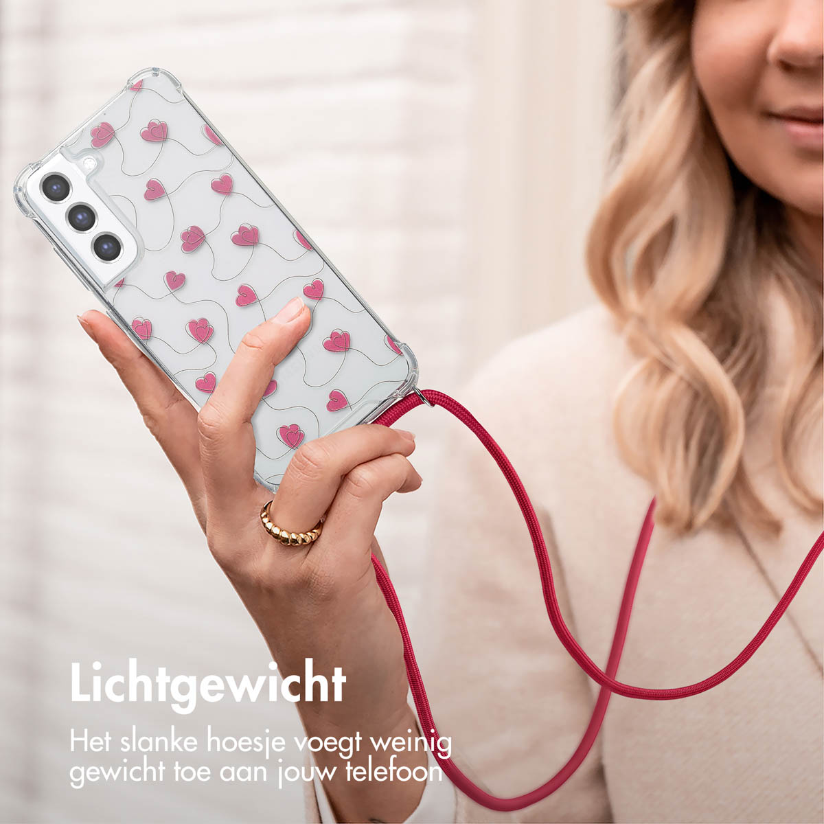 Vrouw houdt telefoon vast met roze hartjes hoesje en rode lanyard.