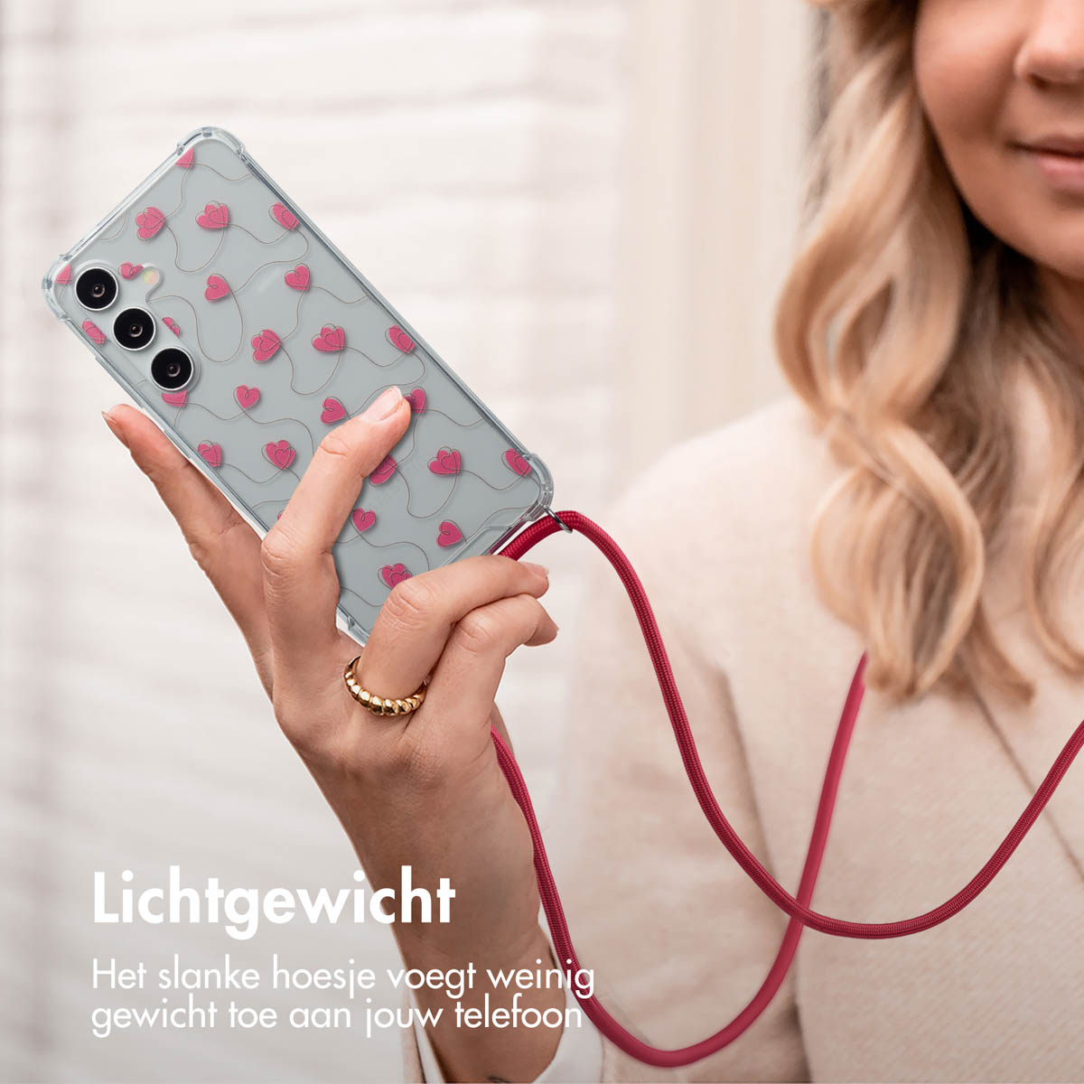 Un téléphone dans un étui transparent avec un motif de cœurs roses, attaché à une lanière rouge.