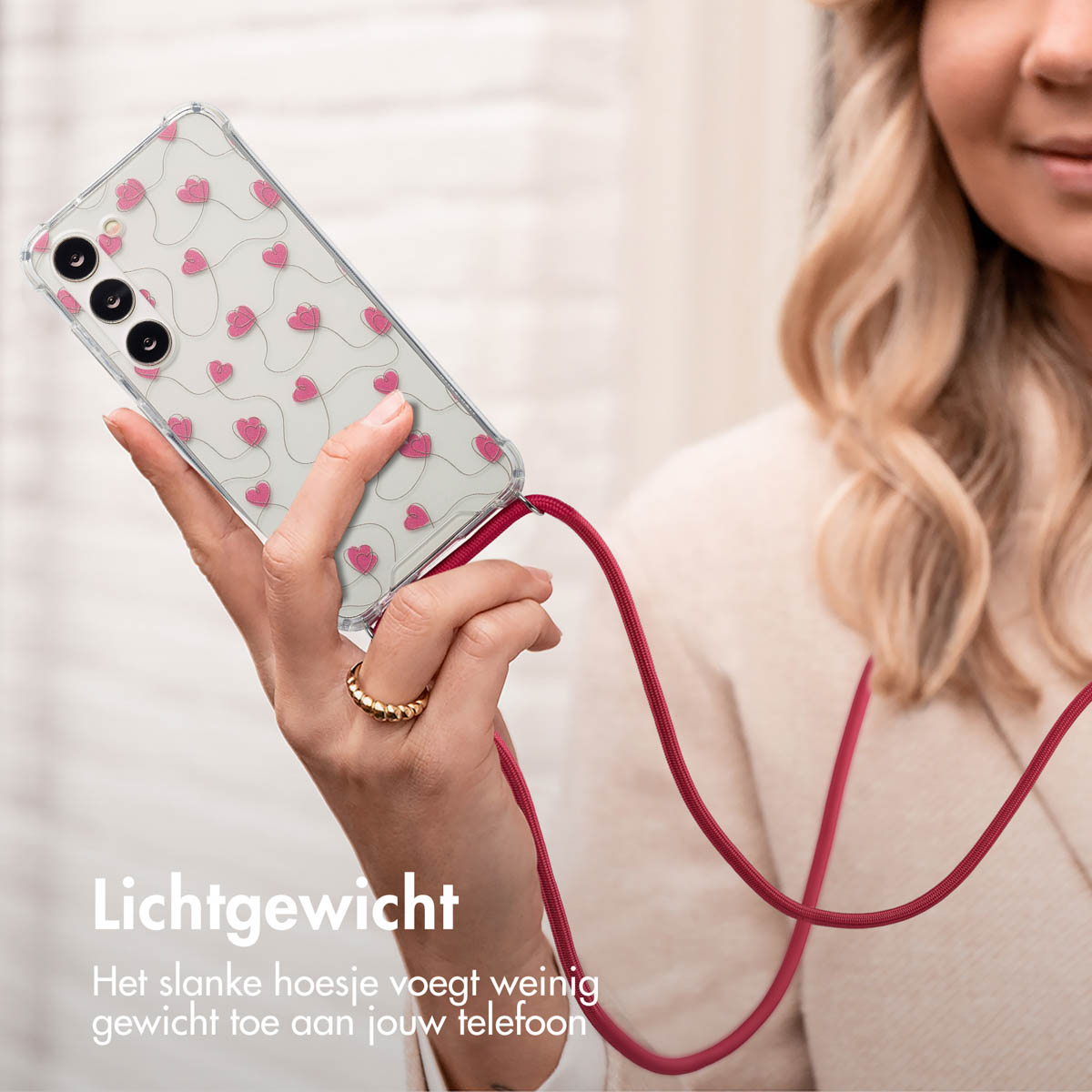 Een vrouw houdt een telefoon met een luipaardprint hoesje en een bruin koord vast. Ze draagt een ring.