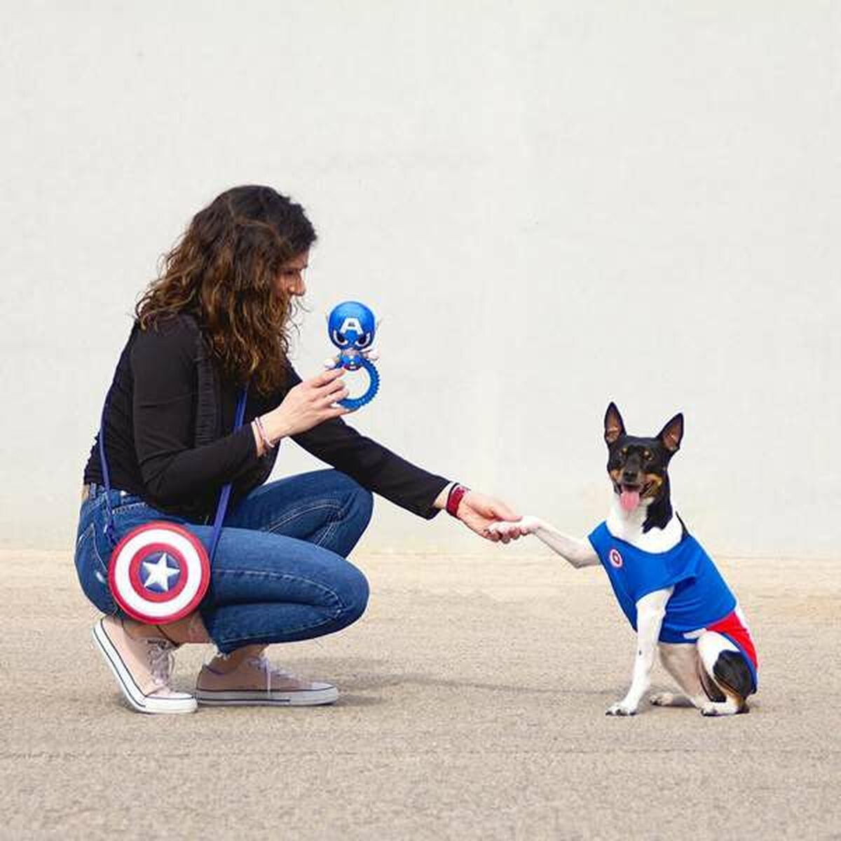 Donna in ginocchio con borsa di Captain America e cane con abito di Captain America, stretta di mano con zampa di cane.