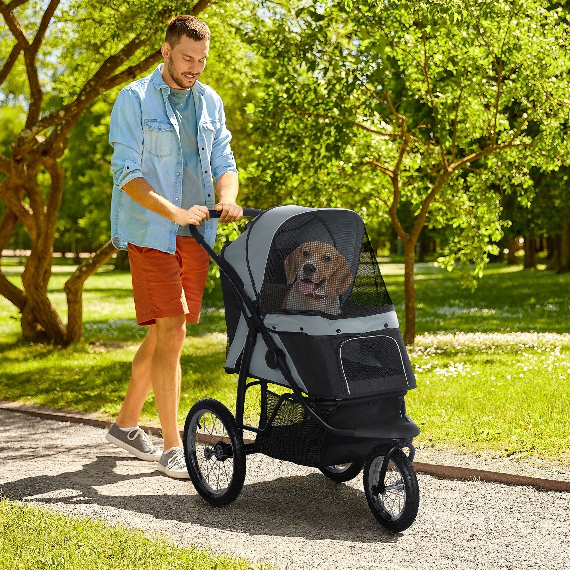Hombre paseando a un perro en un transportín por un camino. El transportín es gris con una malla negra.