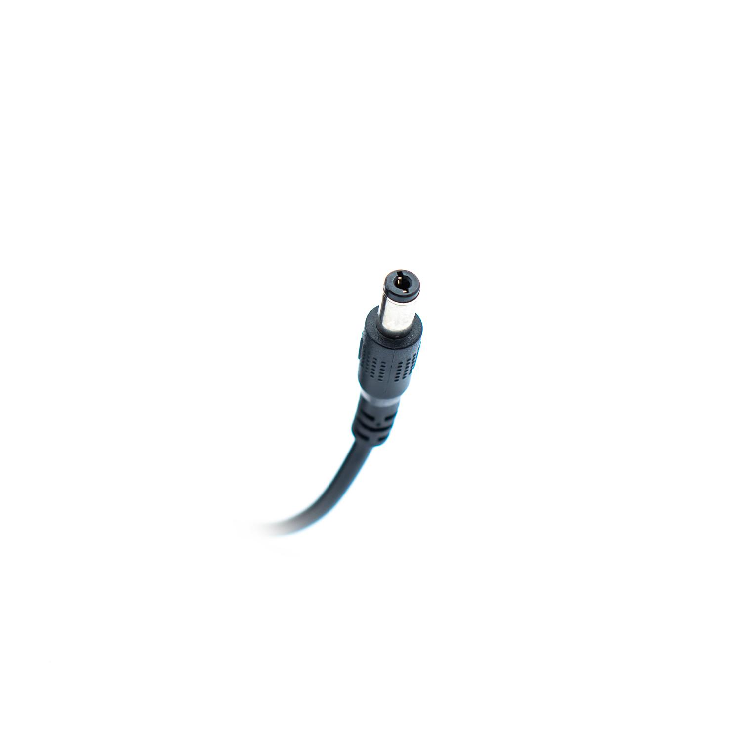 Un adaptador de corriente negro con un conector cilíndrico sobre un fondo blanco. El conector está en la parte superior.