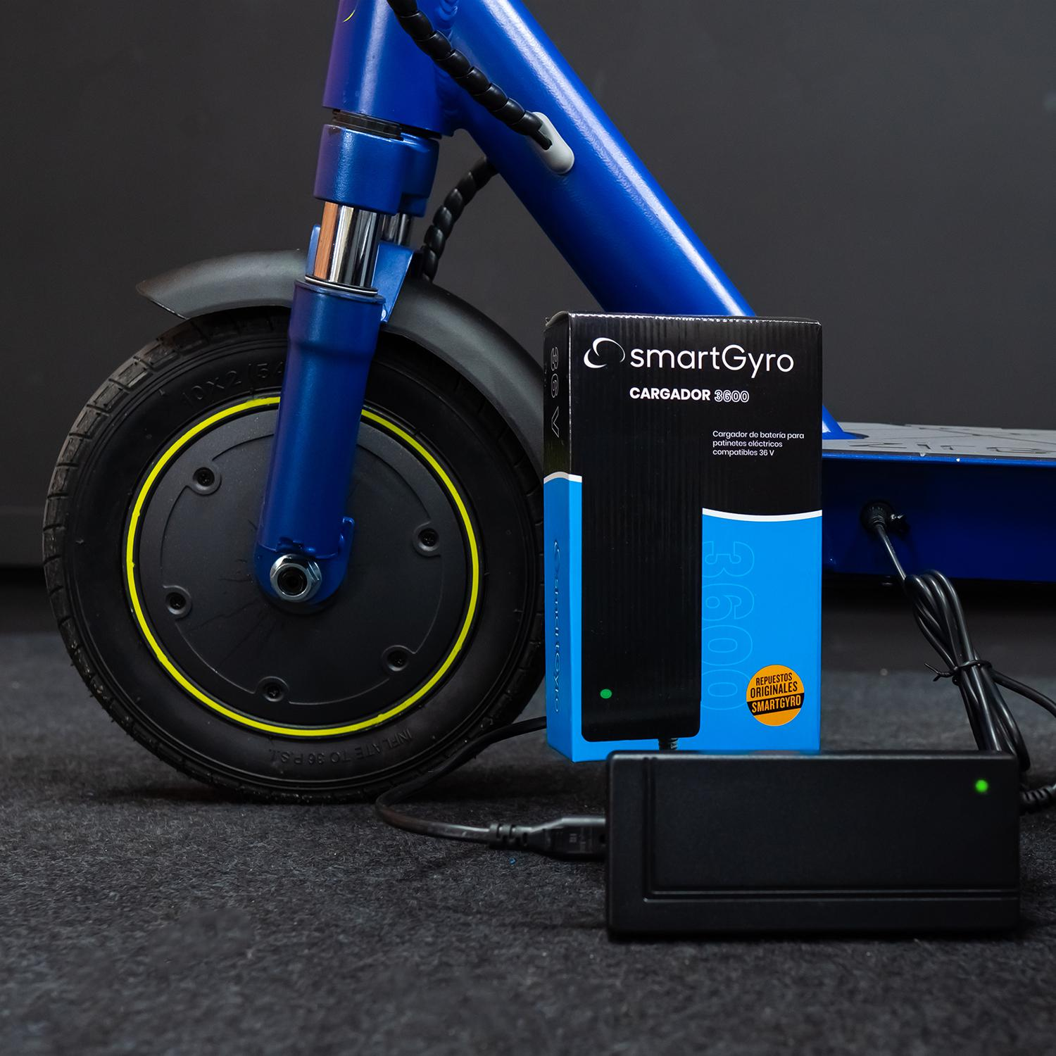 Scooter azul, cargador y caja sobre una superficie oscura. Cargador negro con luz verde.