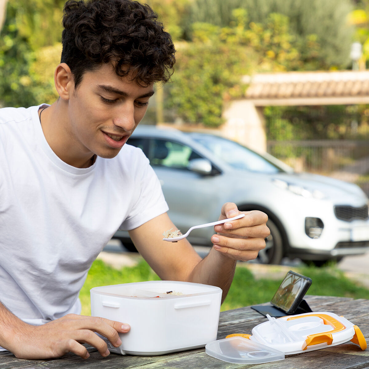 Uomo che mangia cibo da un portapranzo, auto sullo sfondo.