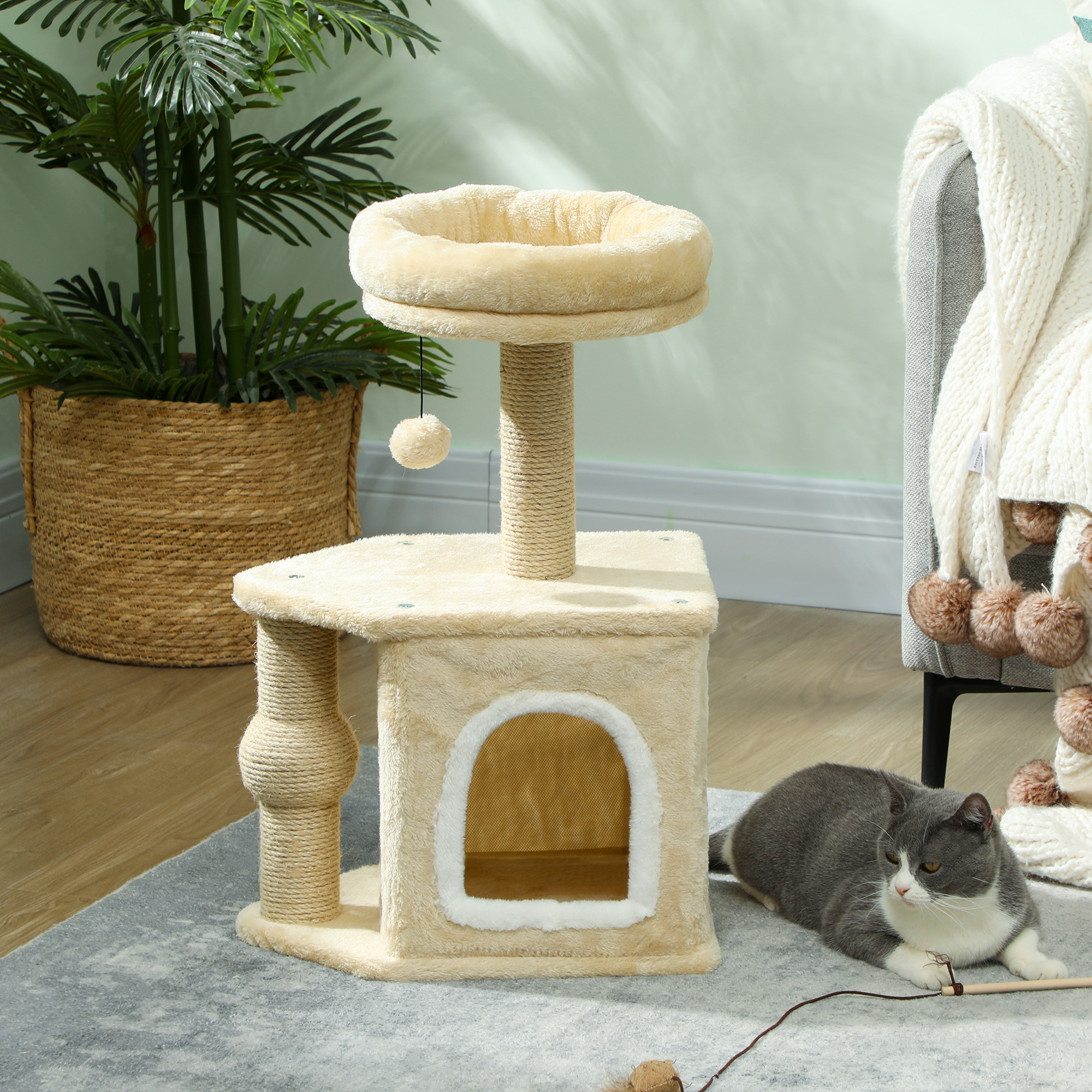 Un gato acostado frente a un árbol para gatos beige, con un fondo de sala de estar.