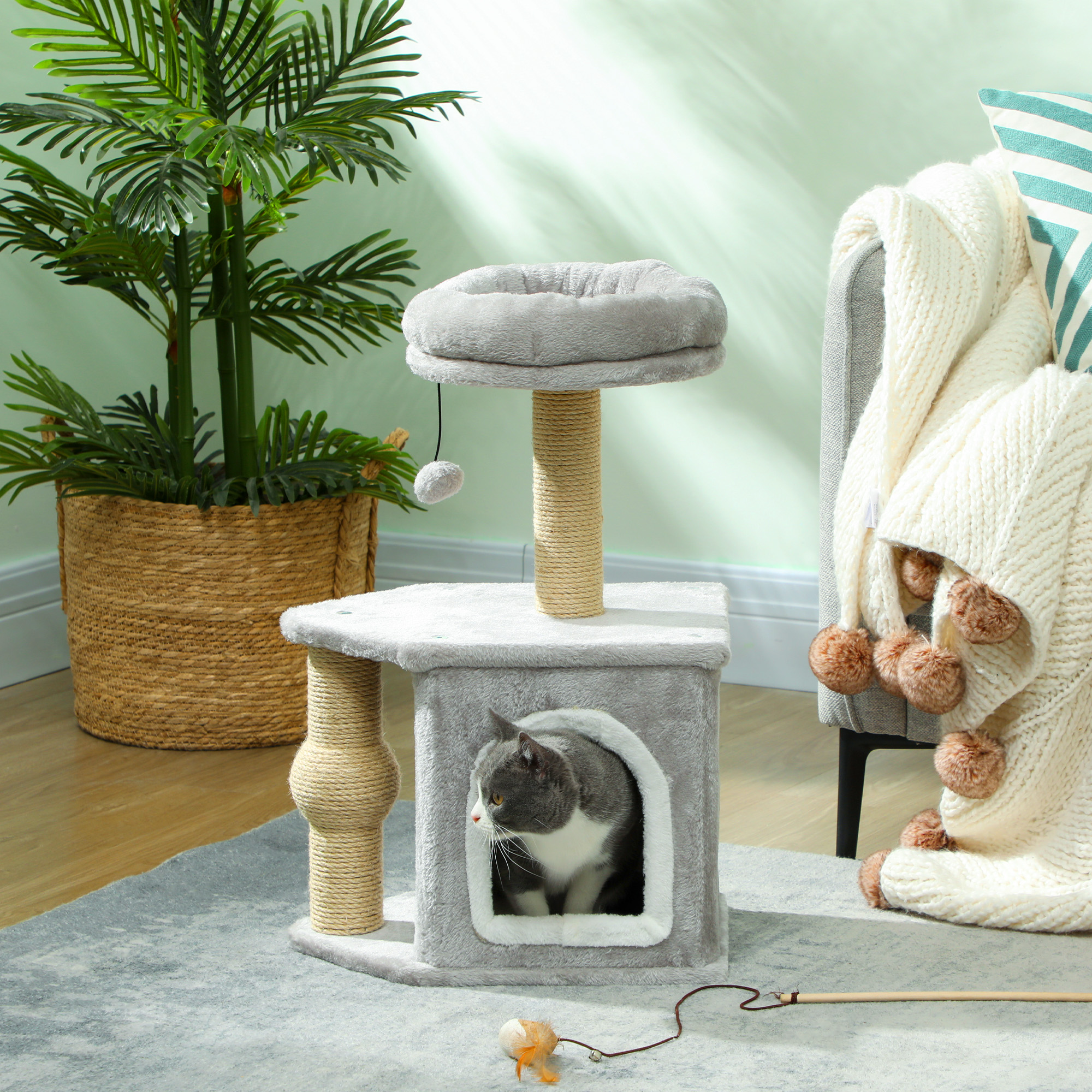 Un árbol para gatos gris con un gato dentro. Un juguete y una planta están en la habitación.