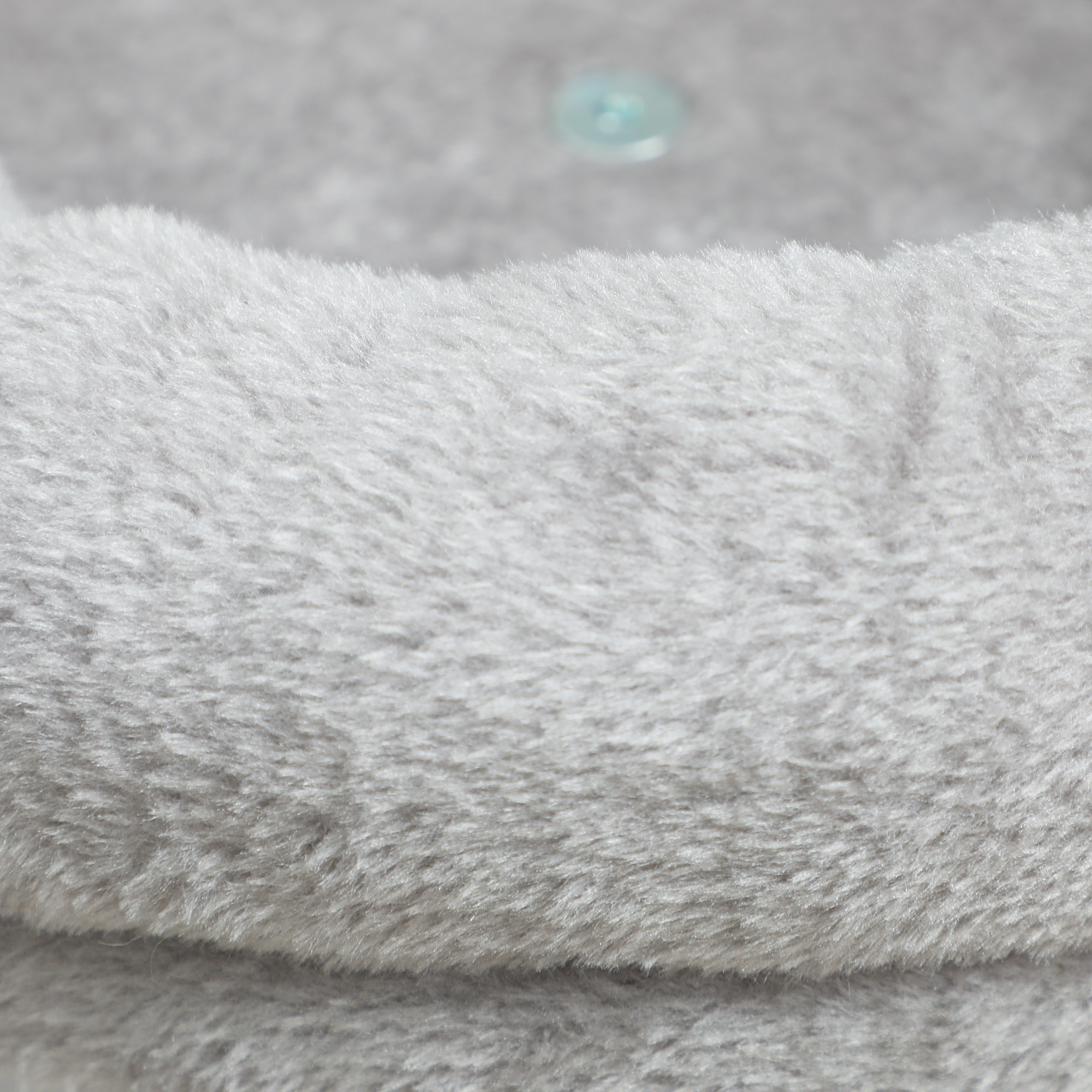 Primer plano de tela de felpa gris suave, posiblemente parte de una cama para gatos, con botón visible.