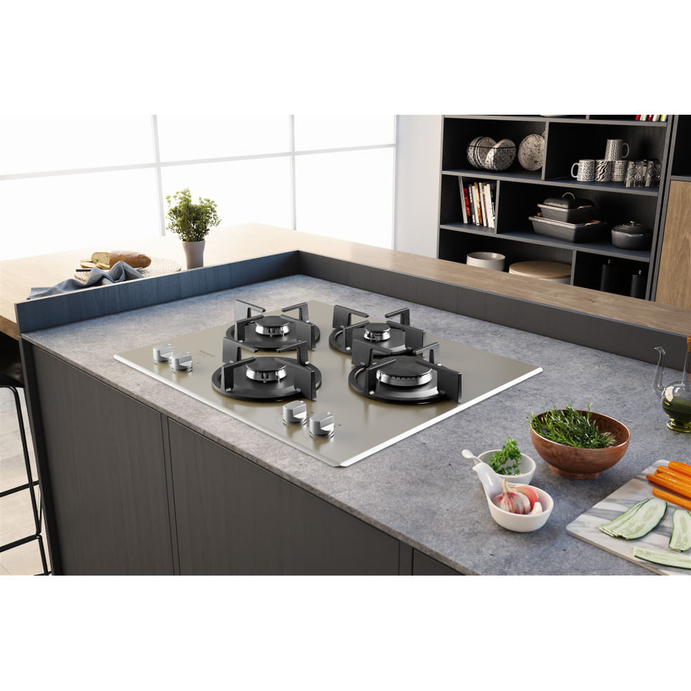 Una cocina con una encimera de gas. Verduras y especias en la encimera. Hay un armario al fondo.