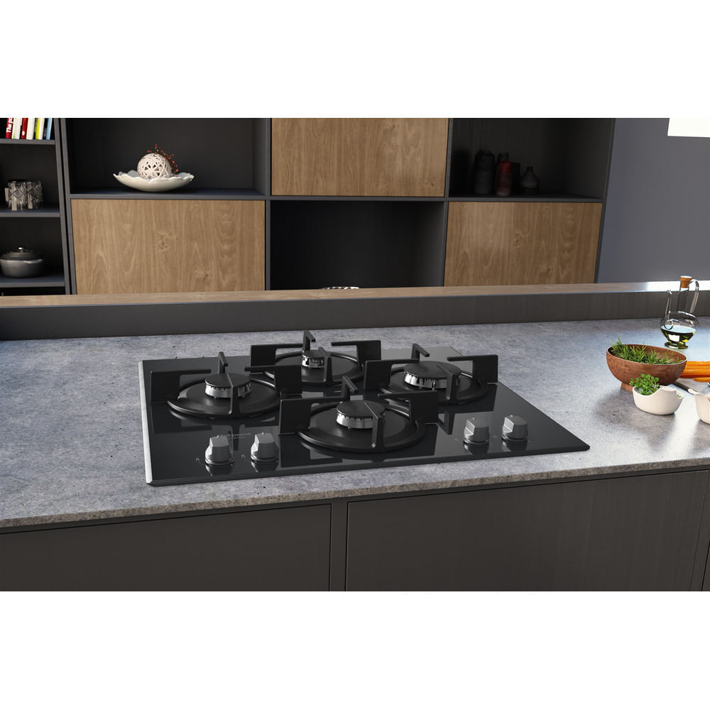 Un piano cottura a gas nero su un piano di lavoro, con armadi e un ambiente cucina sullo sfondo.