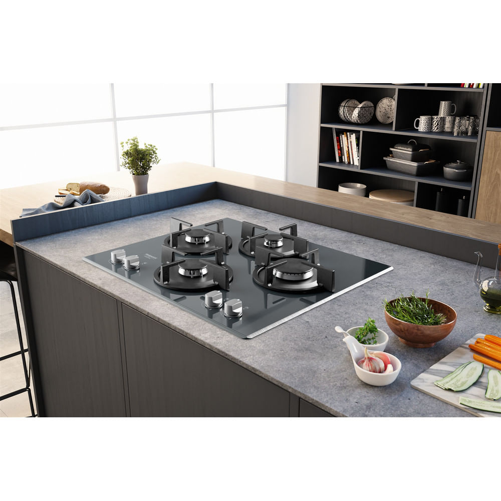 Una cucina con piano cottura a gas. Il piano cottura è nero. Verdure e spezie sul bancone.