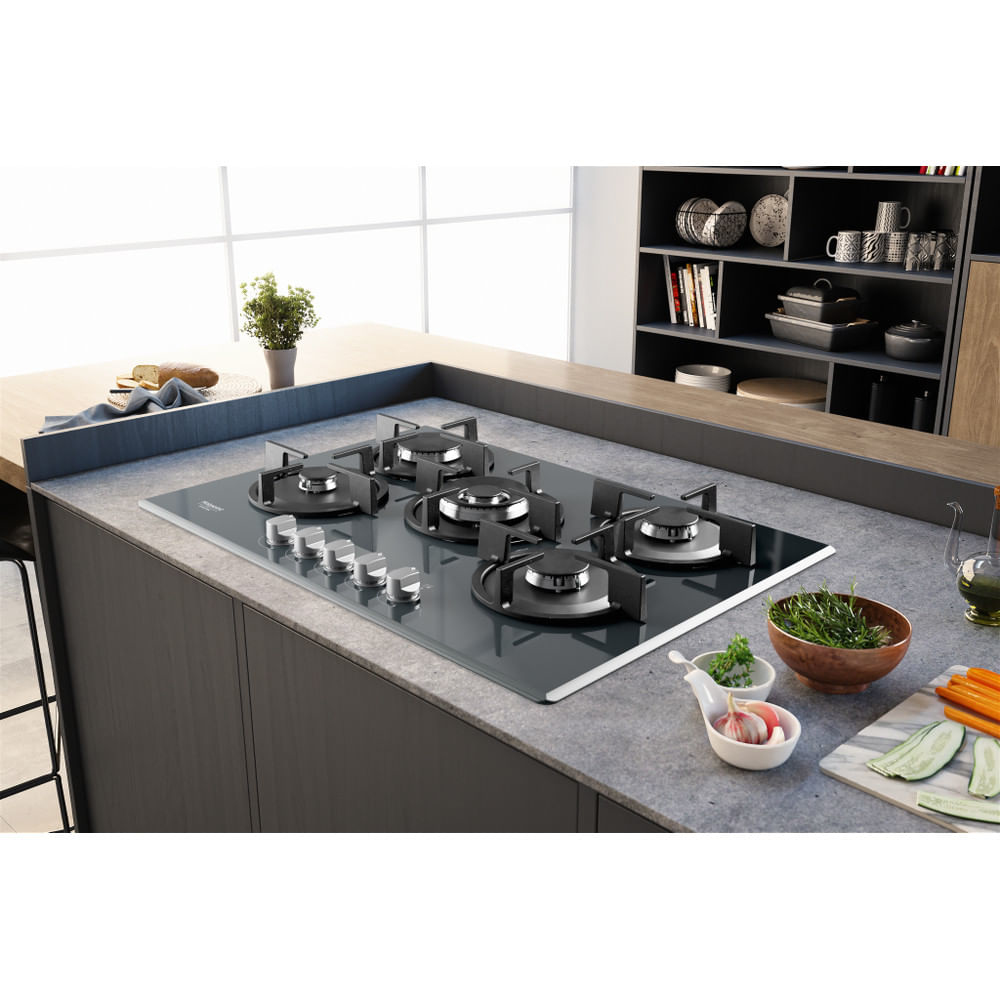 Kuchnia z płytą gazową. Płyta jest czarna. Warzywa i przyprawy na blacie.