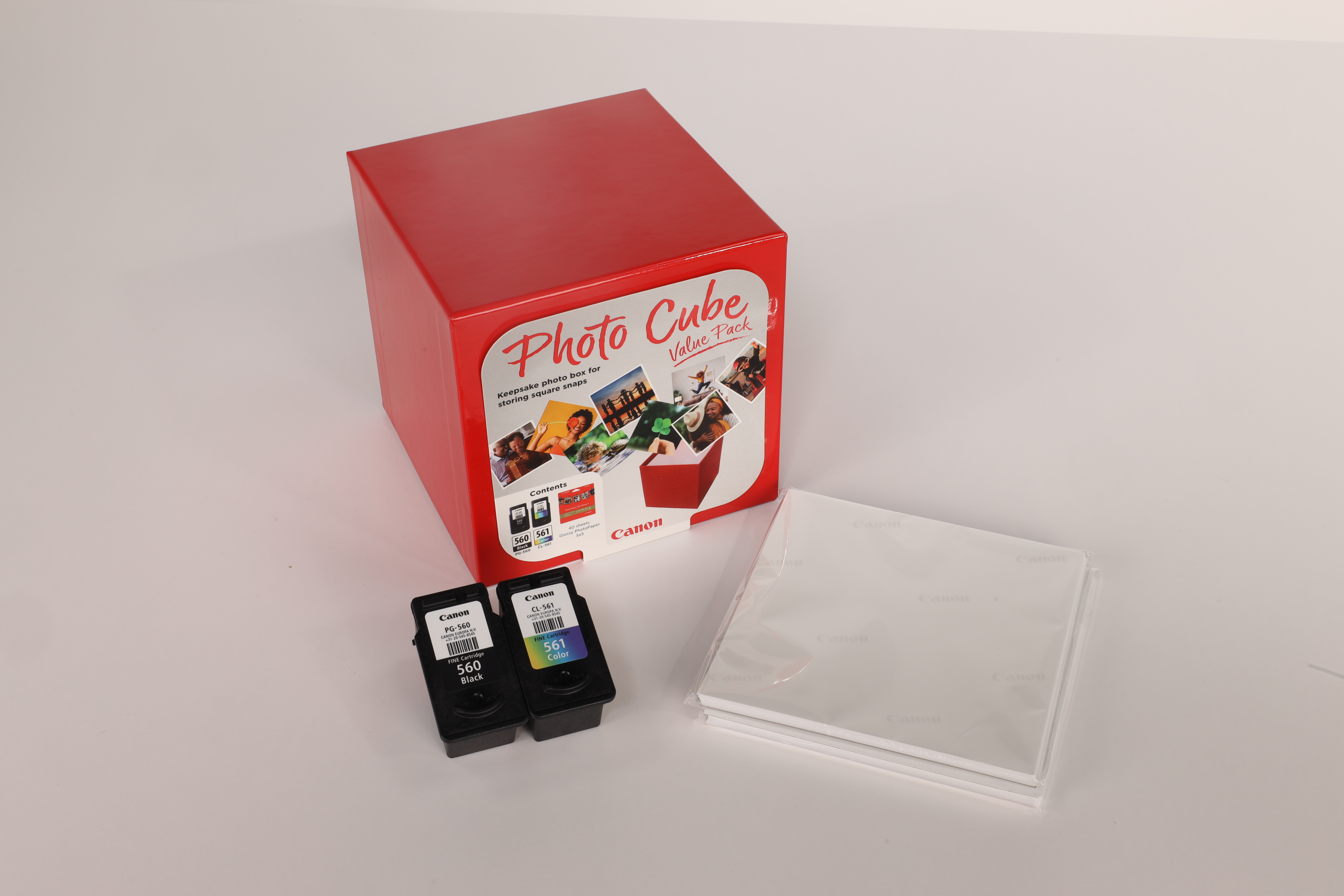 A red Photo Cube box, two ink cartridges, and paper are on a white surface.