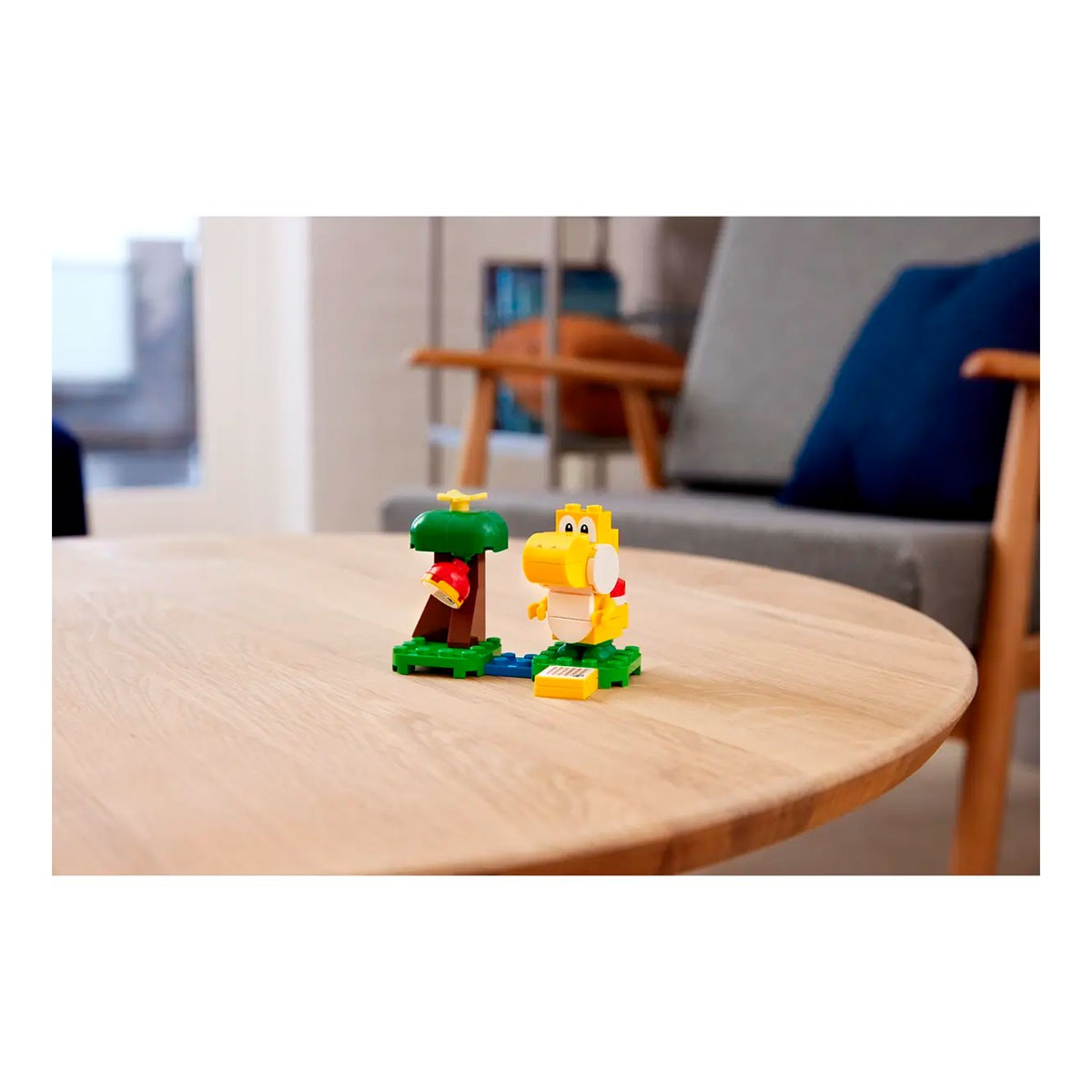 Set Lego con una figura di Yoshi giallo, un albero con una mela rossa e una piattaforma verde. Su un tavolo di legno.