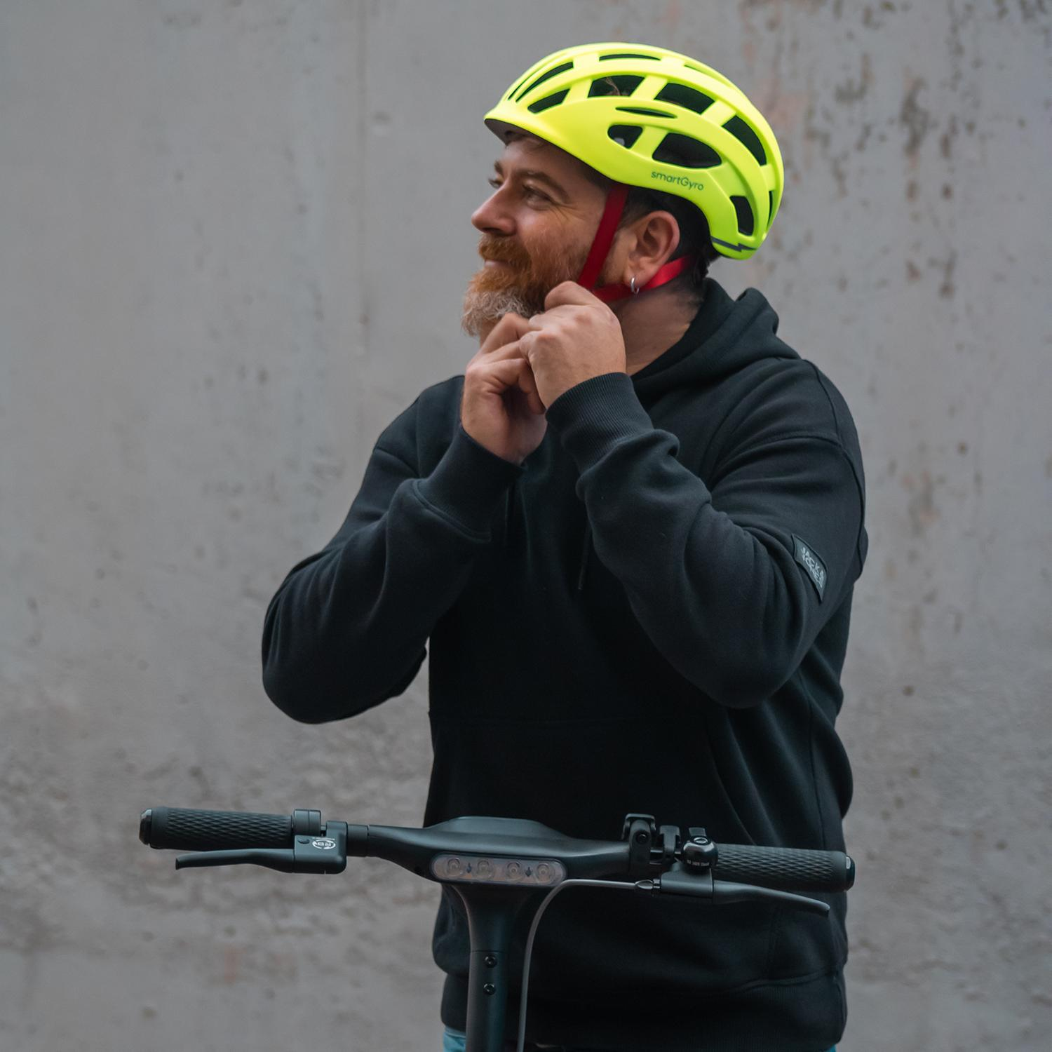 Un hombre con barba, con una sudadera con capucha negra y un casco de bicicleta amarillo, ajustando las correas.