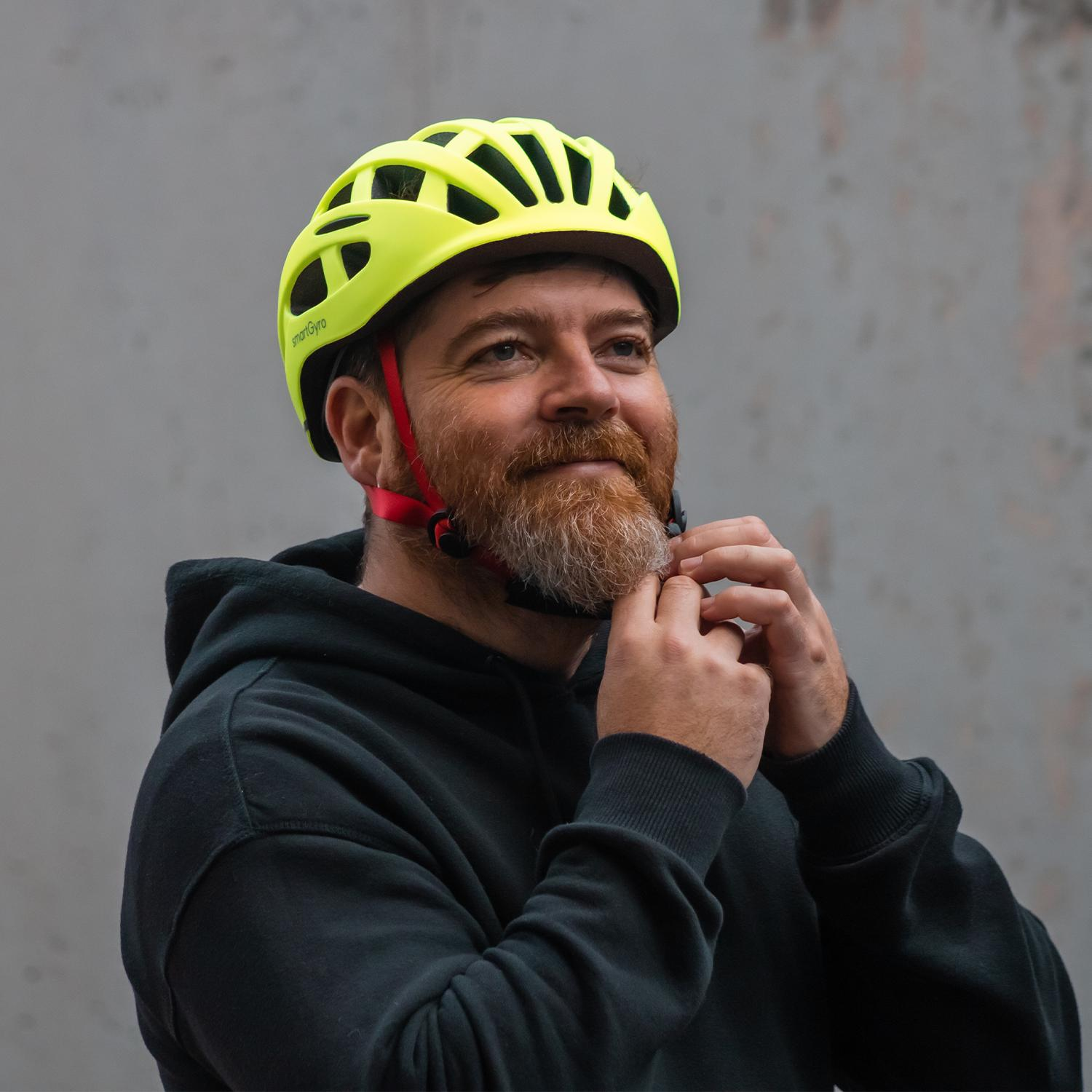 Un hombre con barba, con una sudadera con capucha negra y un casco de bicicleta amarillo, mirando hacia arriba.