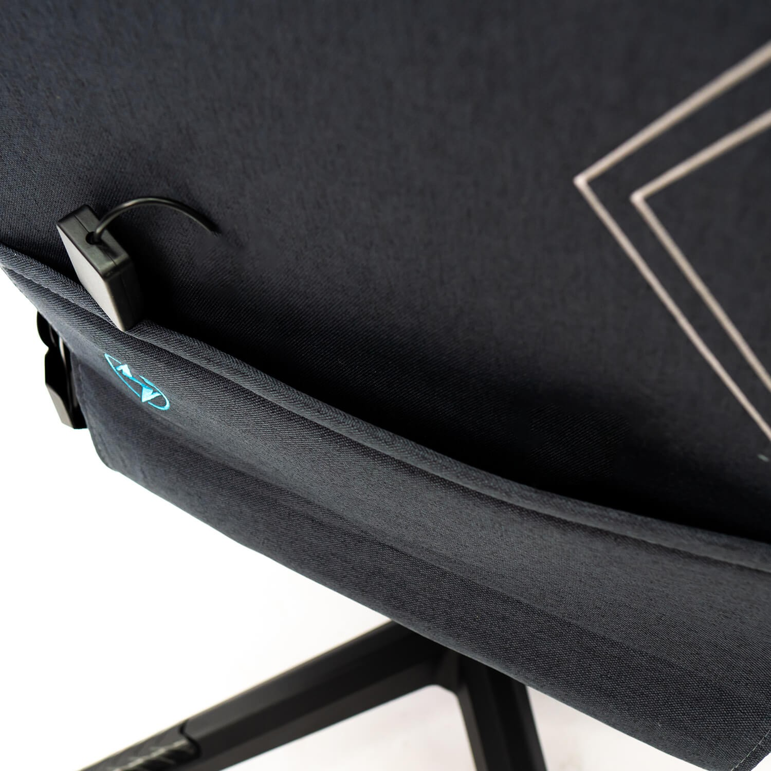 Primer plano del bolsillo trasero de una silla gaming. Un pequeño dispositivo negro es visible.
