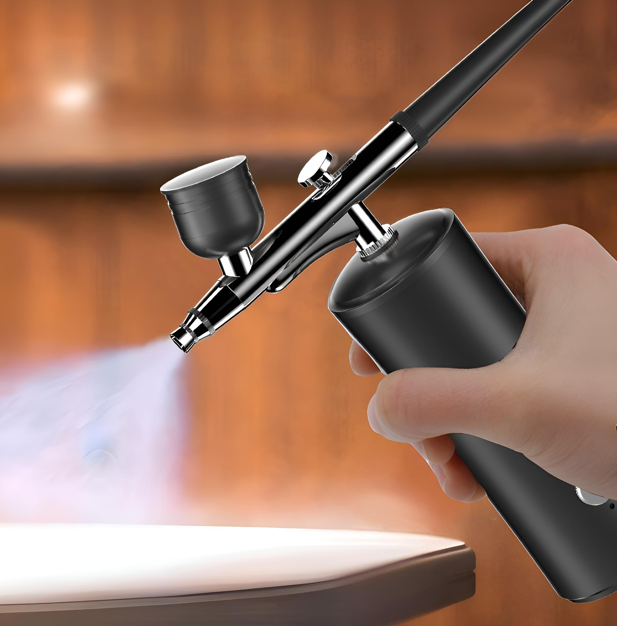 Eine Hand hält eine schwarz-silberne Airbrush, die Nebel sprüht. Ein verschwommener Hintergrund aus Holzmöbeln.