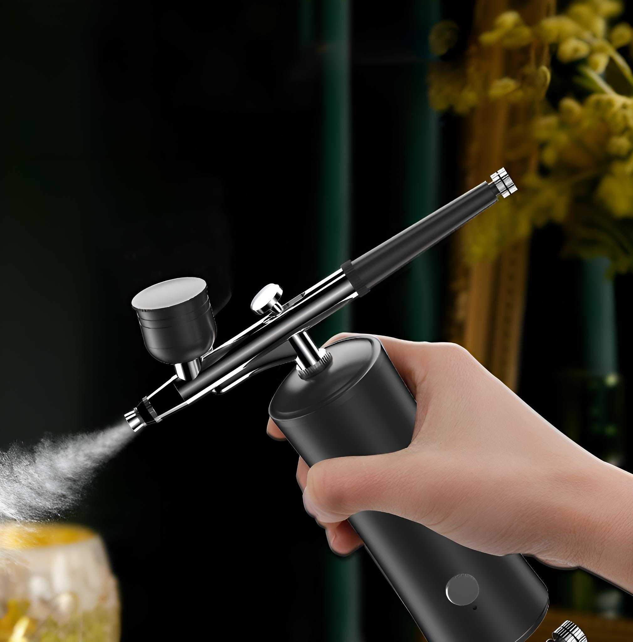 Eine Hand hält eine schwarze Airbrush, die Nebel sprüht. Der Hintergrund ist verschwommen dunkelgrün, beleuchtet.