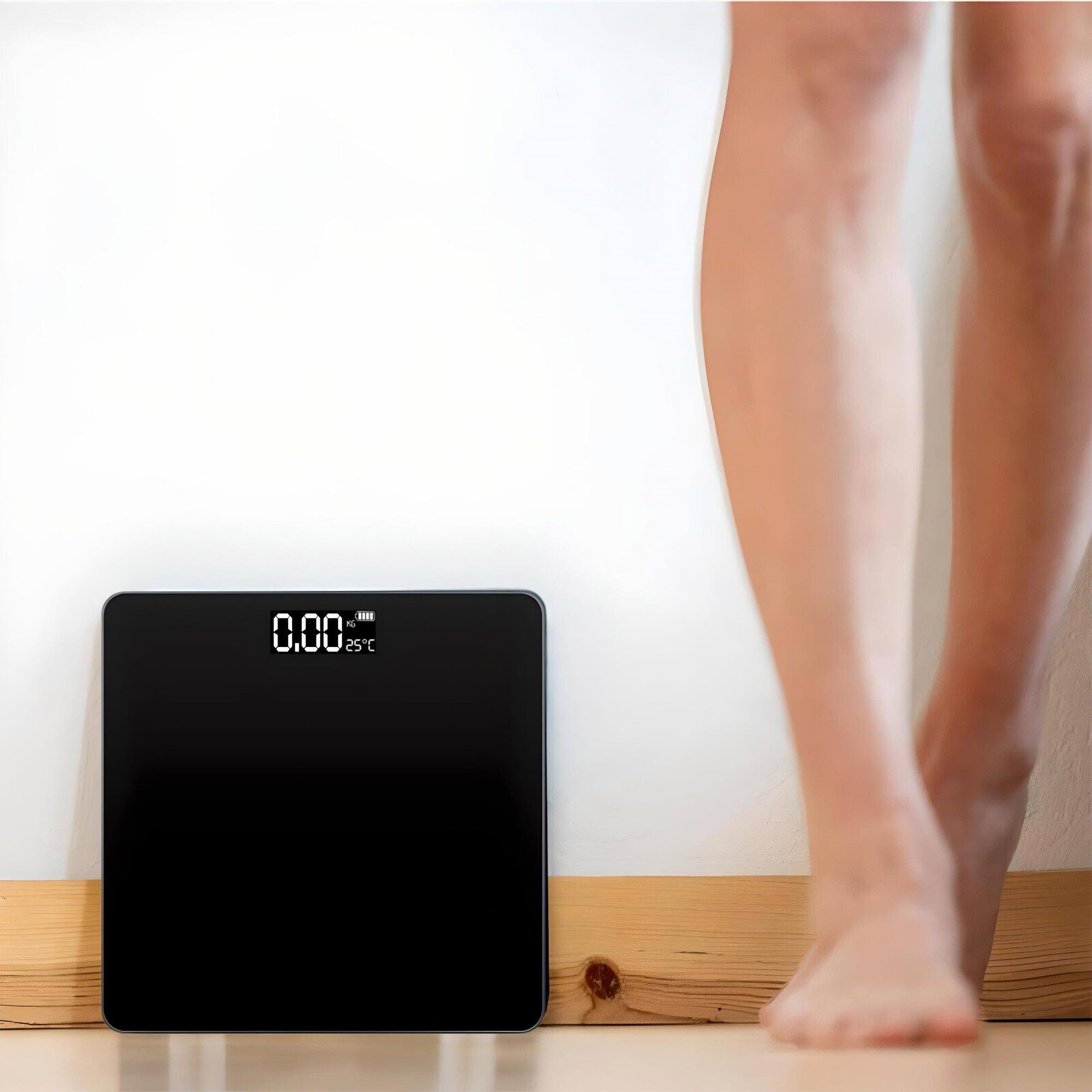 Eine schwarze Digitalwaage auf dem Boden mit Beinen einer Person. Die Waage zeigt 0,00 kg und 25 Grad Celsius an.