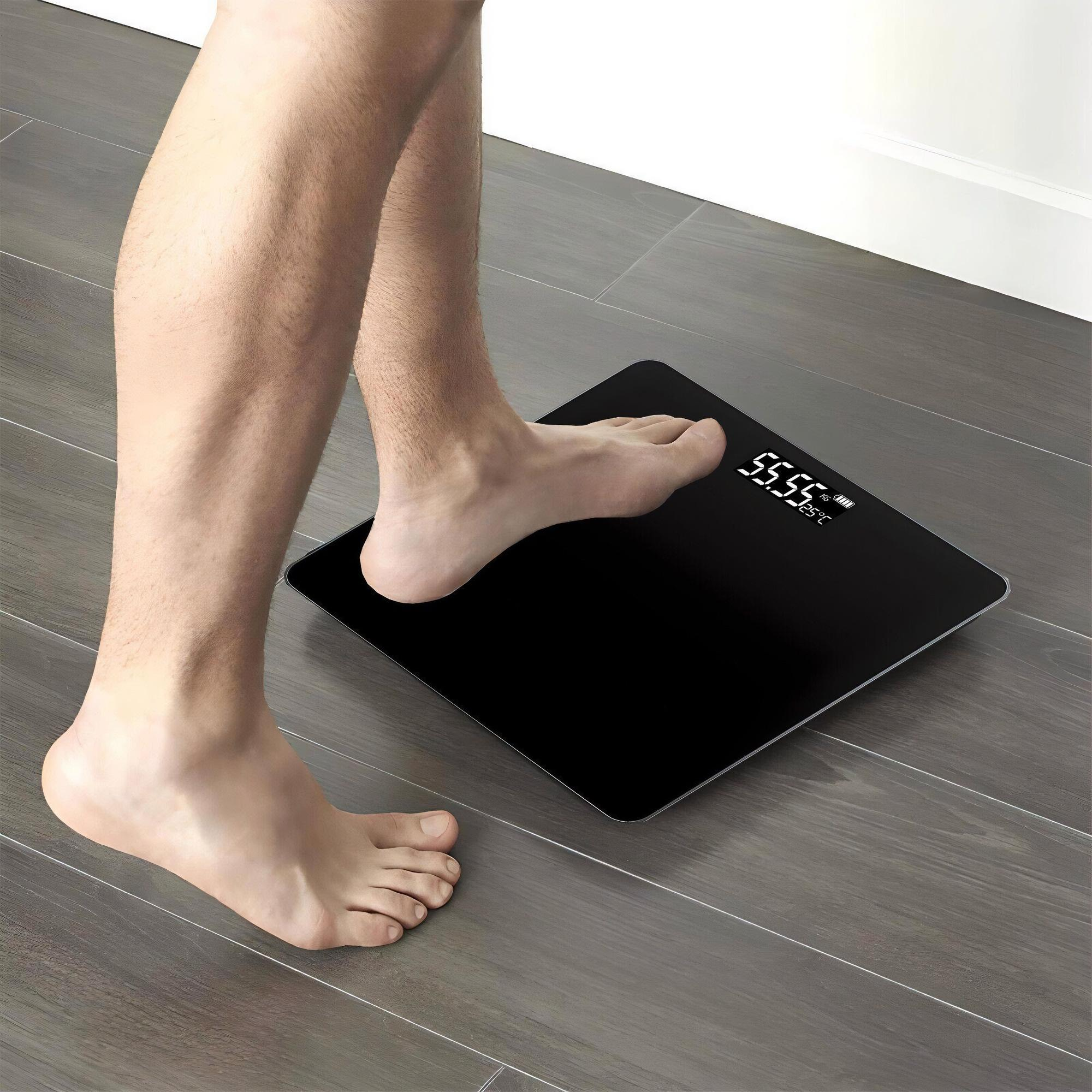 Ein Fuß betritt eine schwarze Digitalwaage. Die Waage zeigt 55,55 kg an.